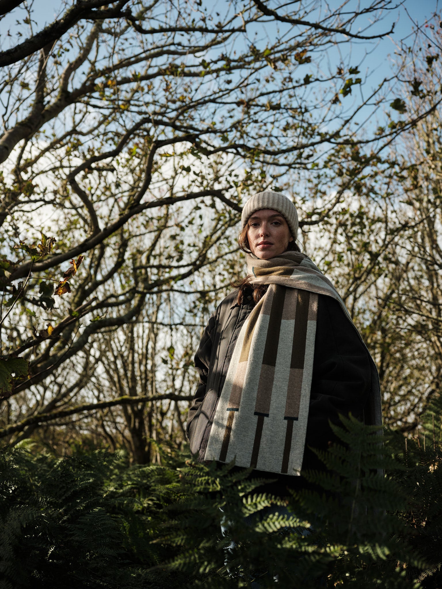 Person wearing a checkered scarf and hat standing in a forest