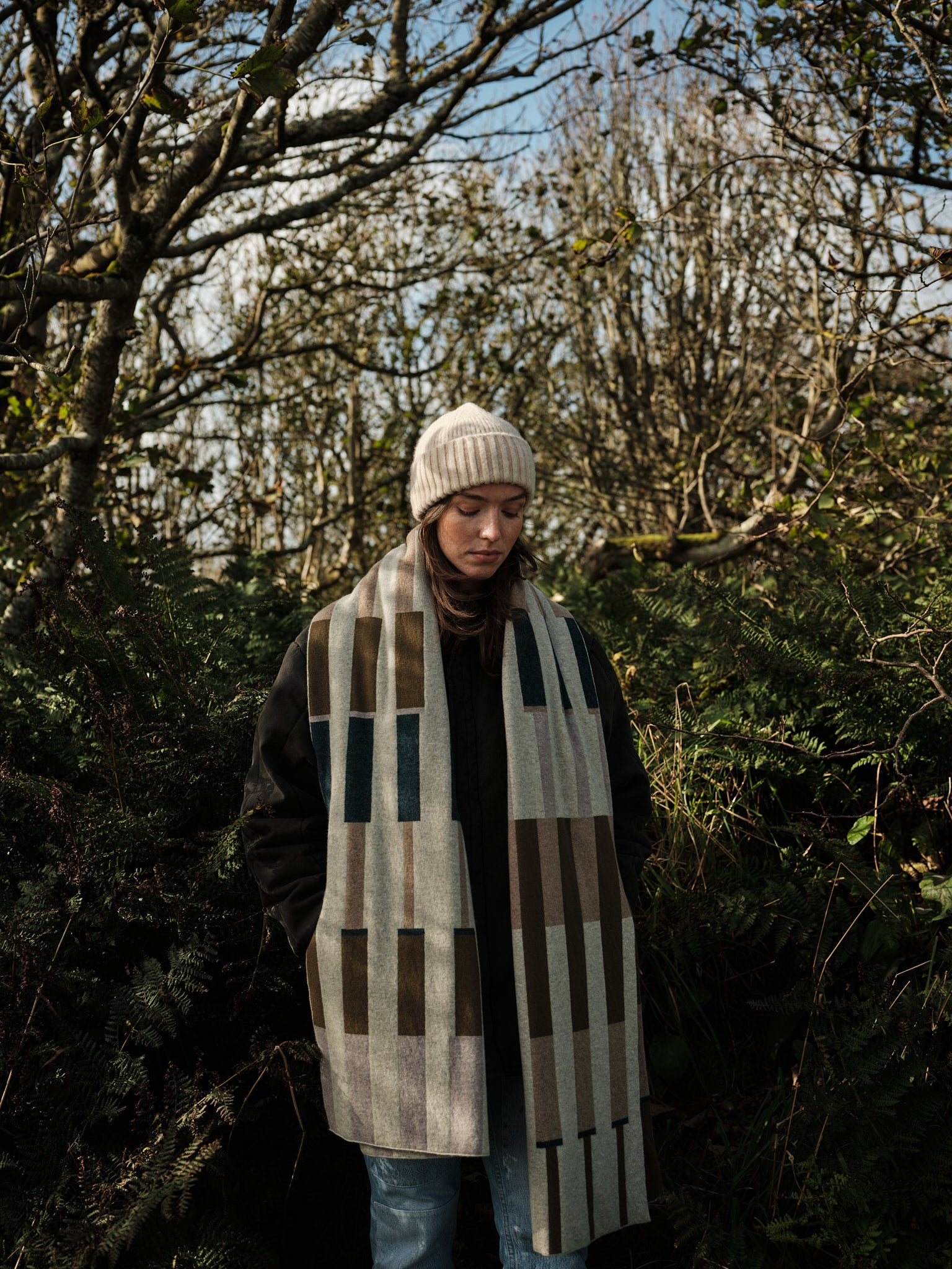 Person wearing a patterned scarf and hat in a forest setting