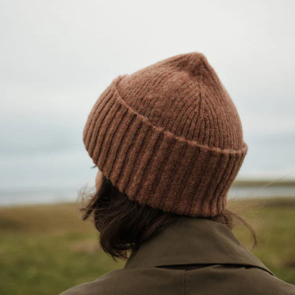 Person wearing a brown knit beanie and coat standing in a field