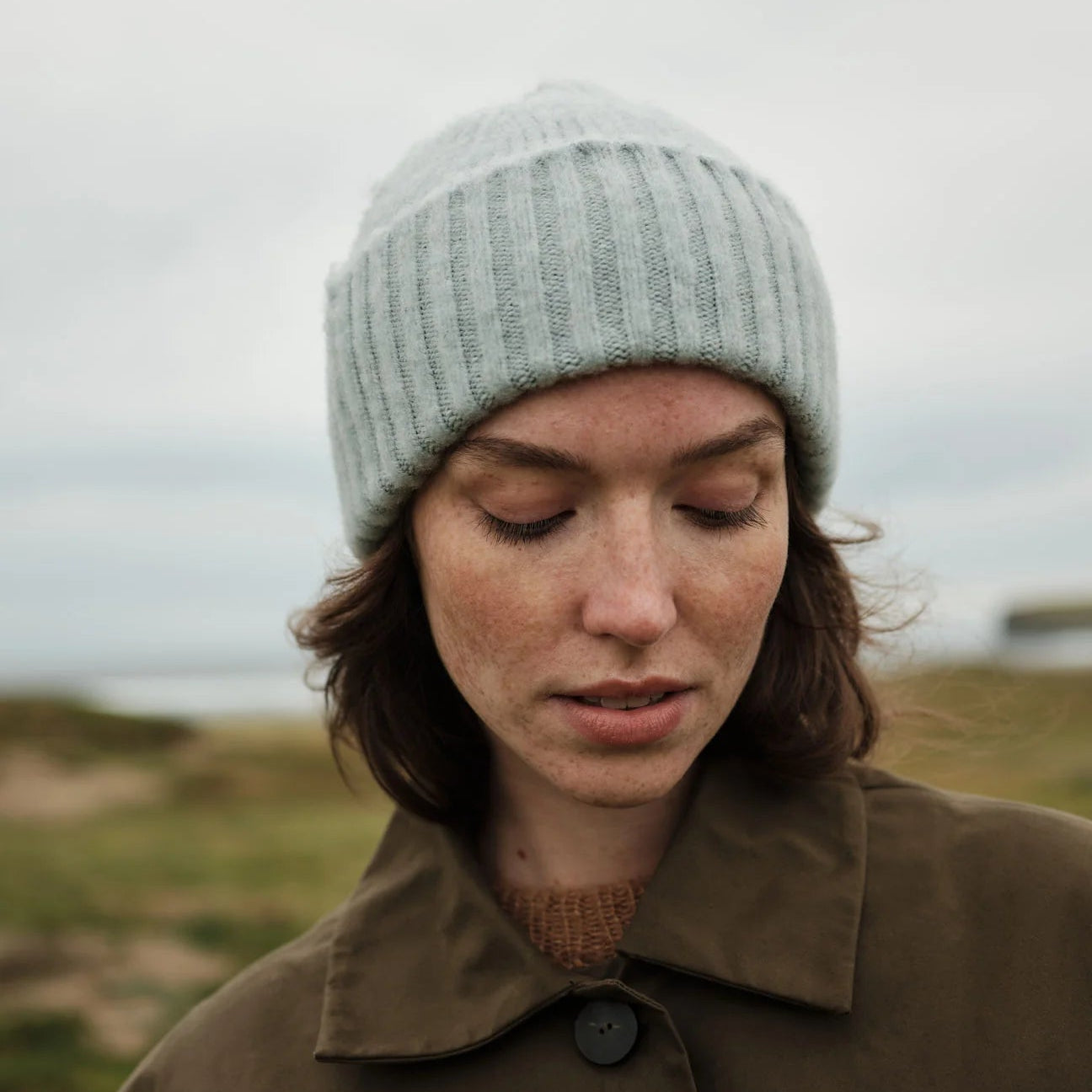 Person wearing a knit beanie and brown coat in a natural setting