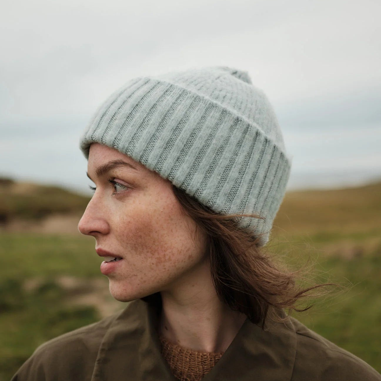 Person wearing a knit hat and brown coat in a grassy field