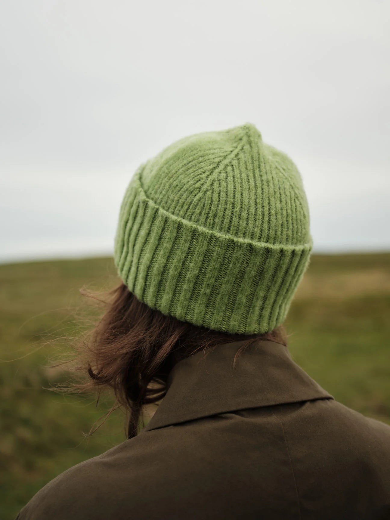 Person wearing a green knitted hat and brown coat in a grassy field