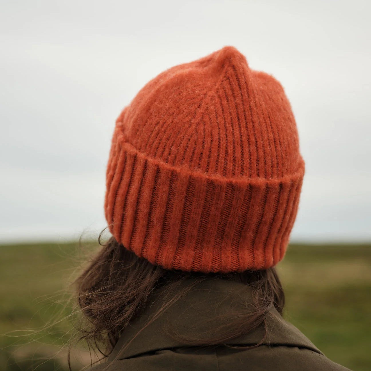 Person wearing an orange knit beanie in a field