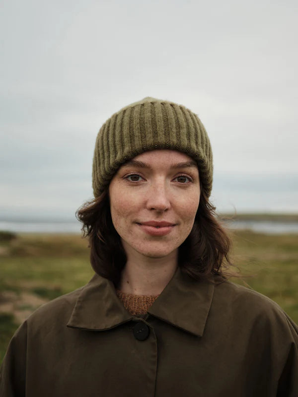 Person wearing a green knitted hat and brown coat in a natural setting