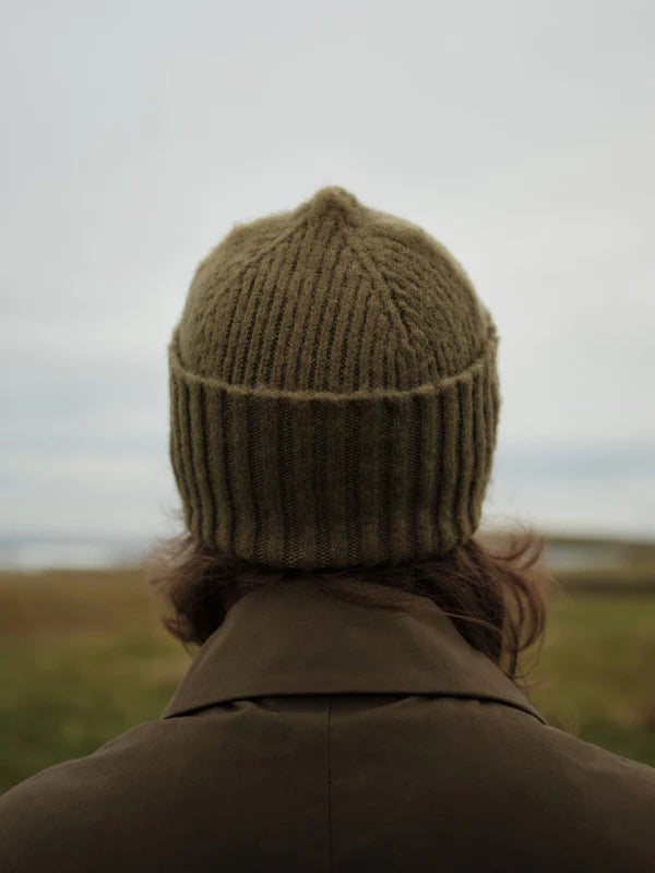 Person wearing a green knitted hat and coat standing in a field with a blurred background