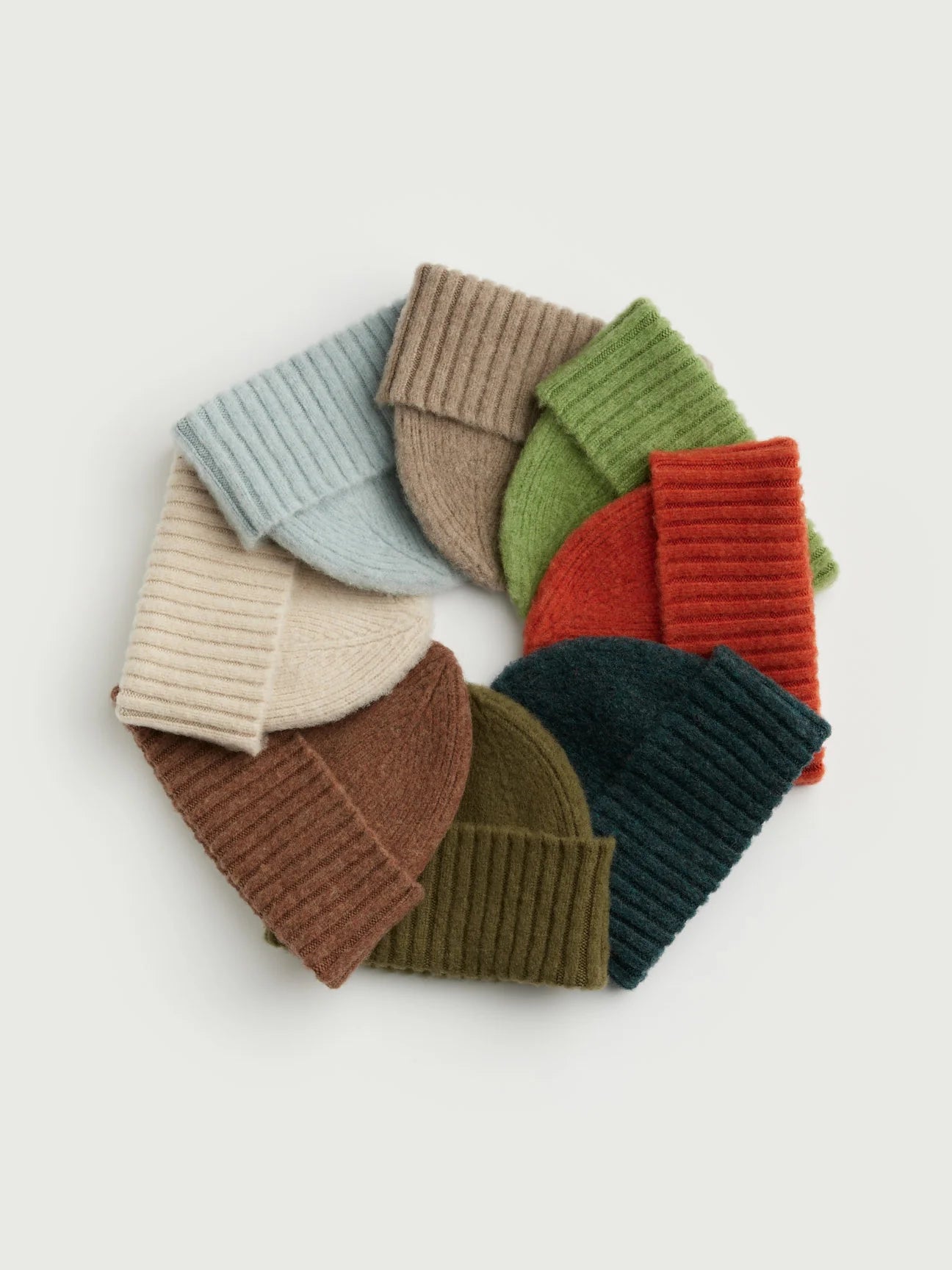Set of colorful knit beanie hats arranged in a circular pattern on a light background