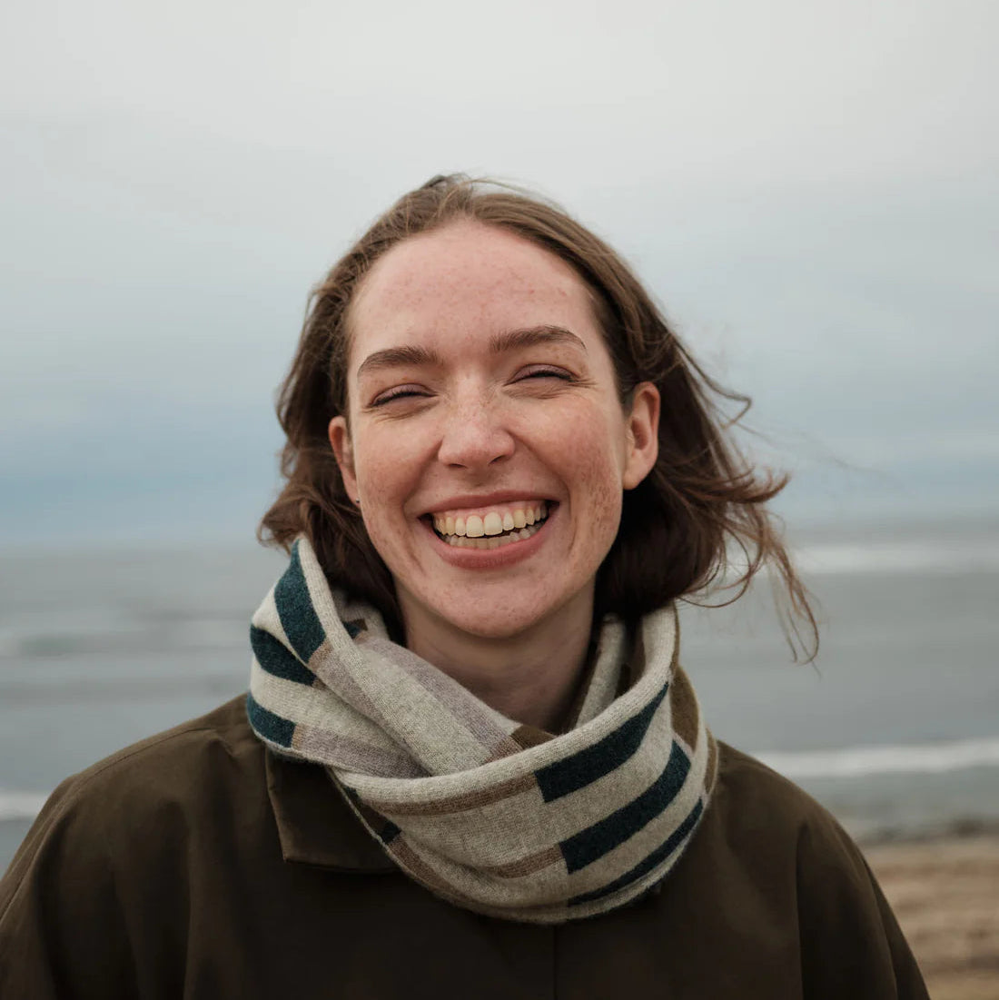 Person wearing a scarf and coat on a beach with a neutral background