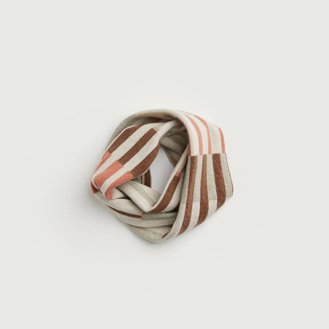 A striped knit scarf in beige, brown, and muted pink, styled in a loose coil on a light gray background.