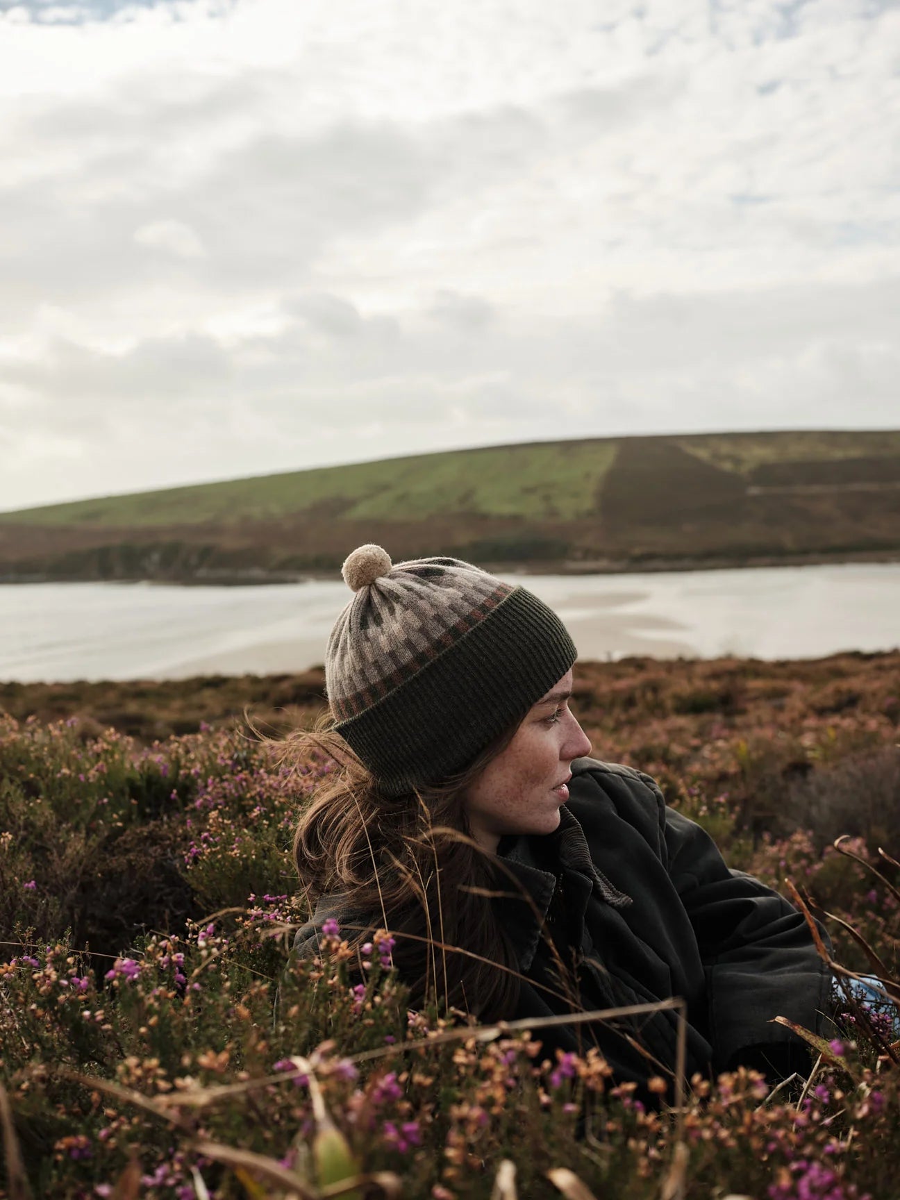 Person sitting in a field with a lake and hills in the background