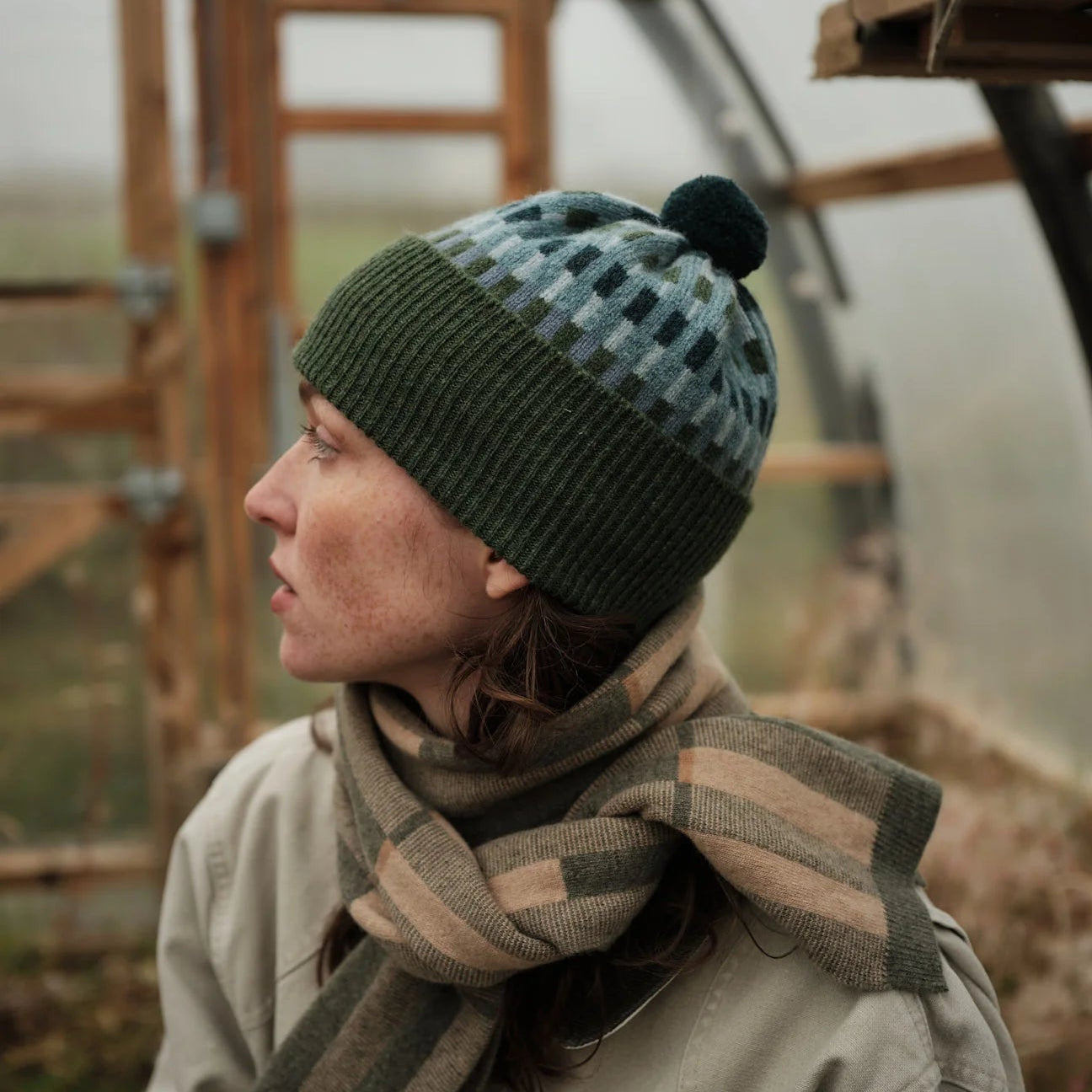 Person wearing a patterned knit hat and scarf in a rustic setting