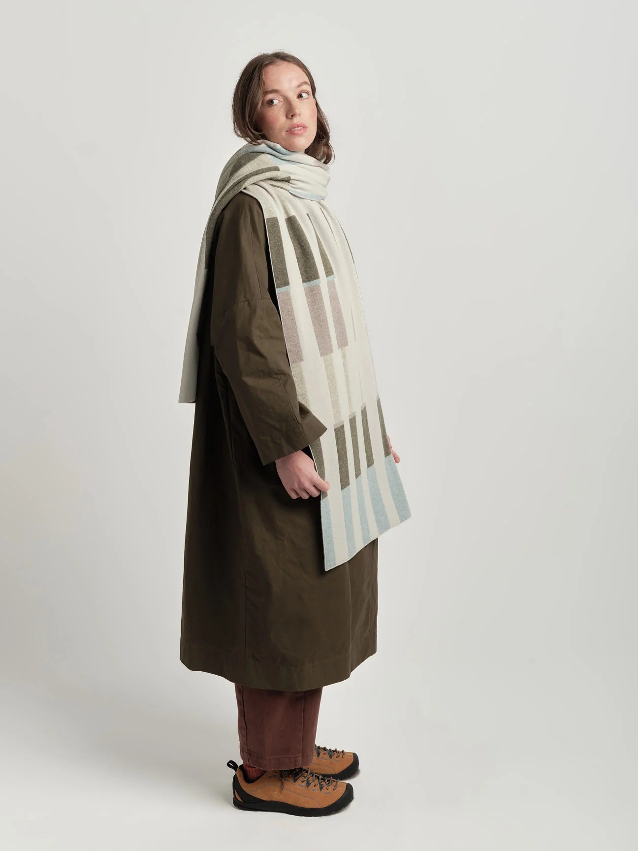 Person wearing a long coat and a patterned scarf on a white background