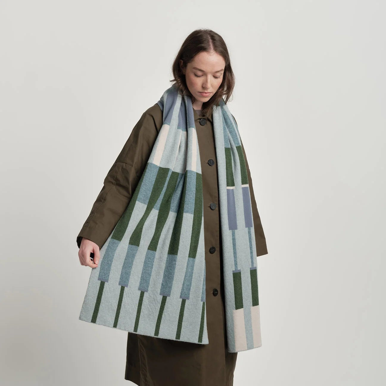 Person wearing a long coat with a patterned scarf on a plain background