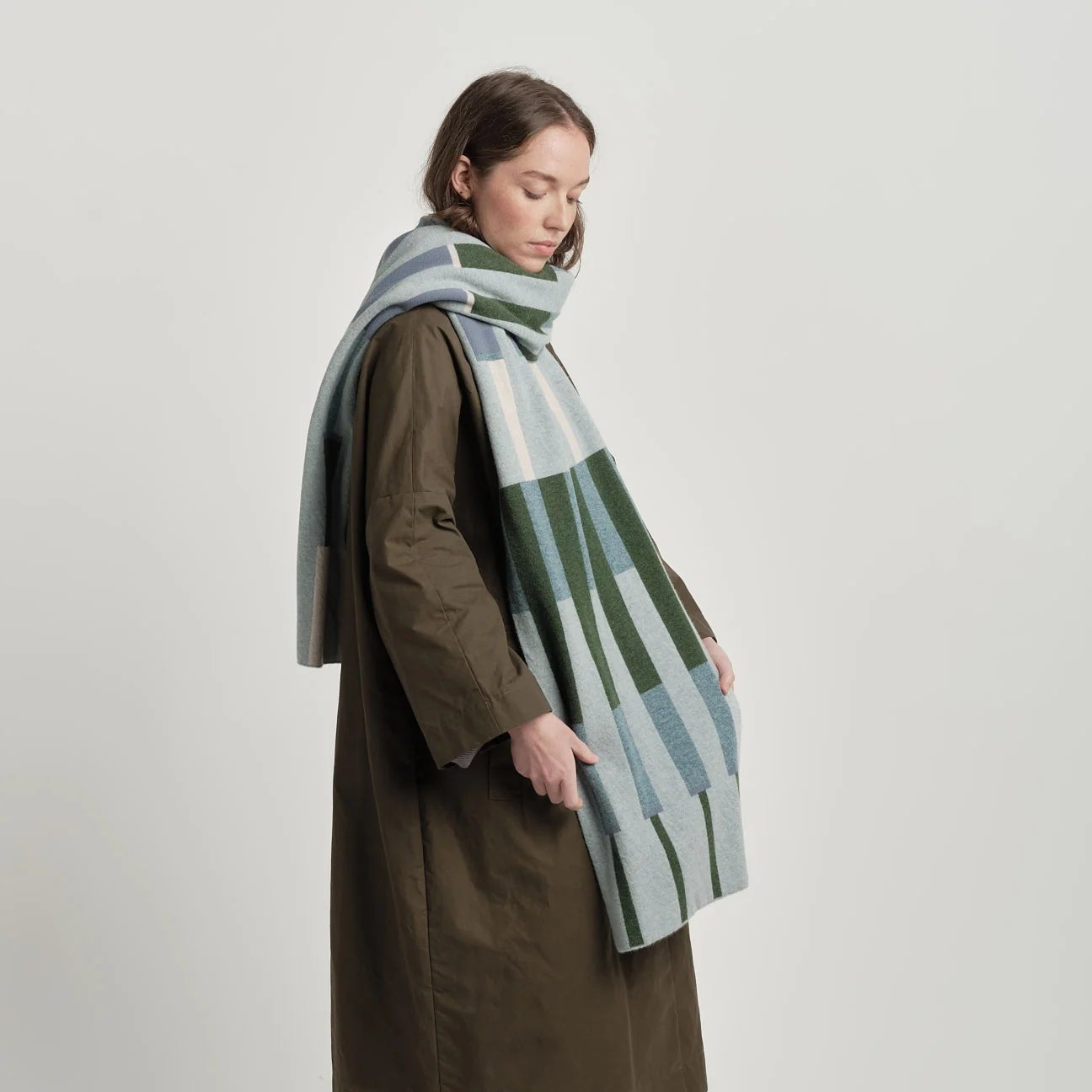 Person wearing a patterned scarf and brown coat on a plain background