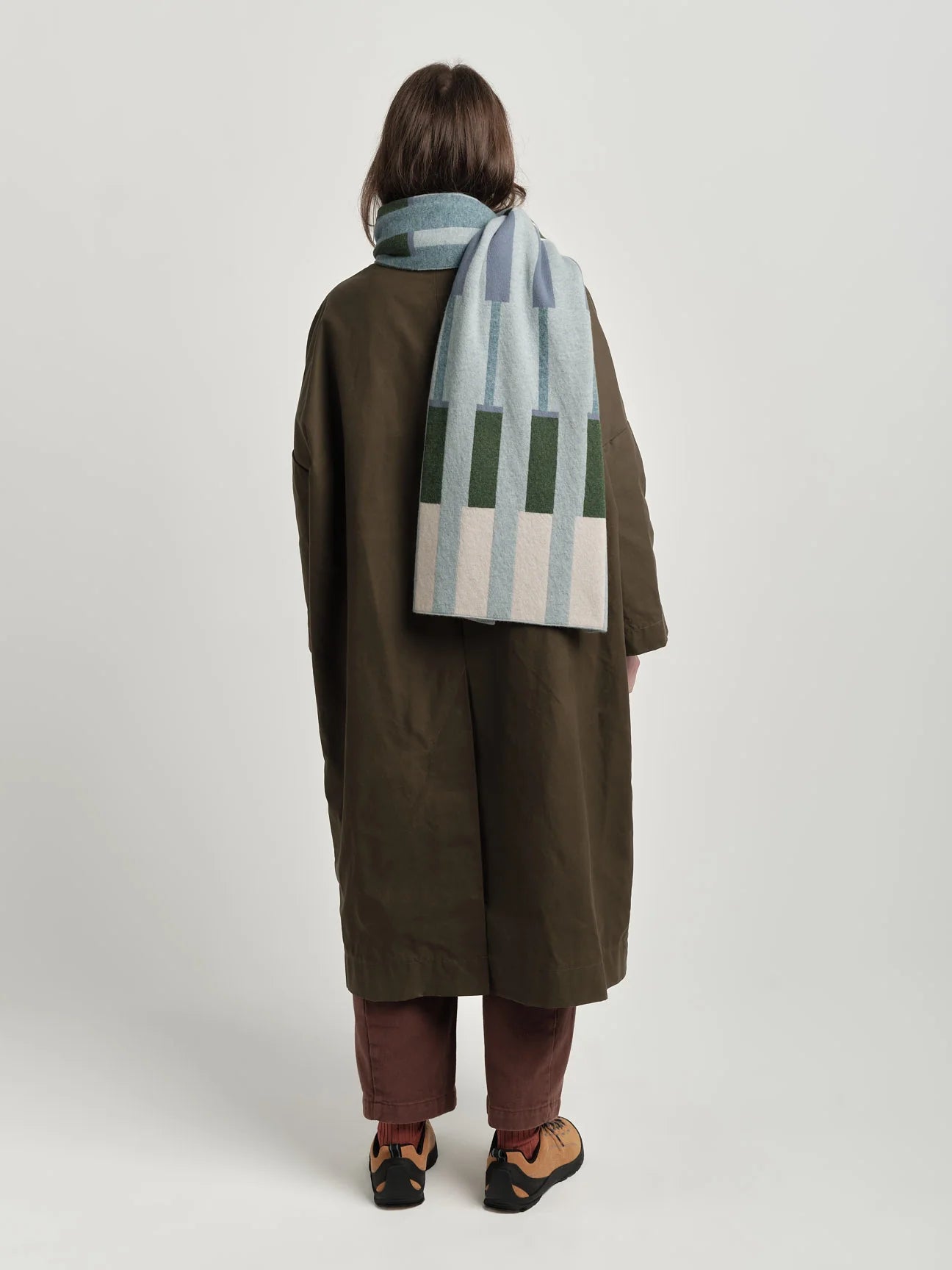 Person wearing a long coat and striped scarf on a plain background