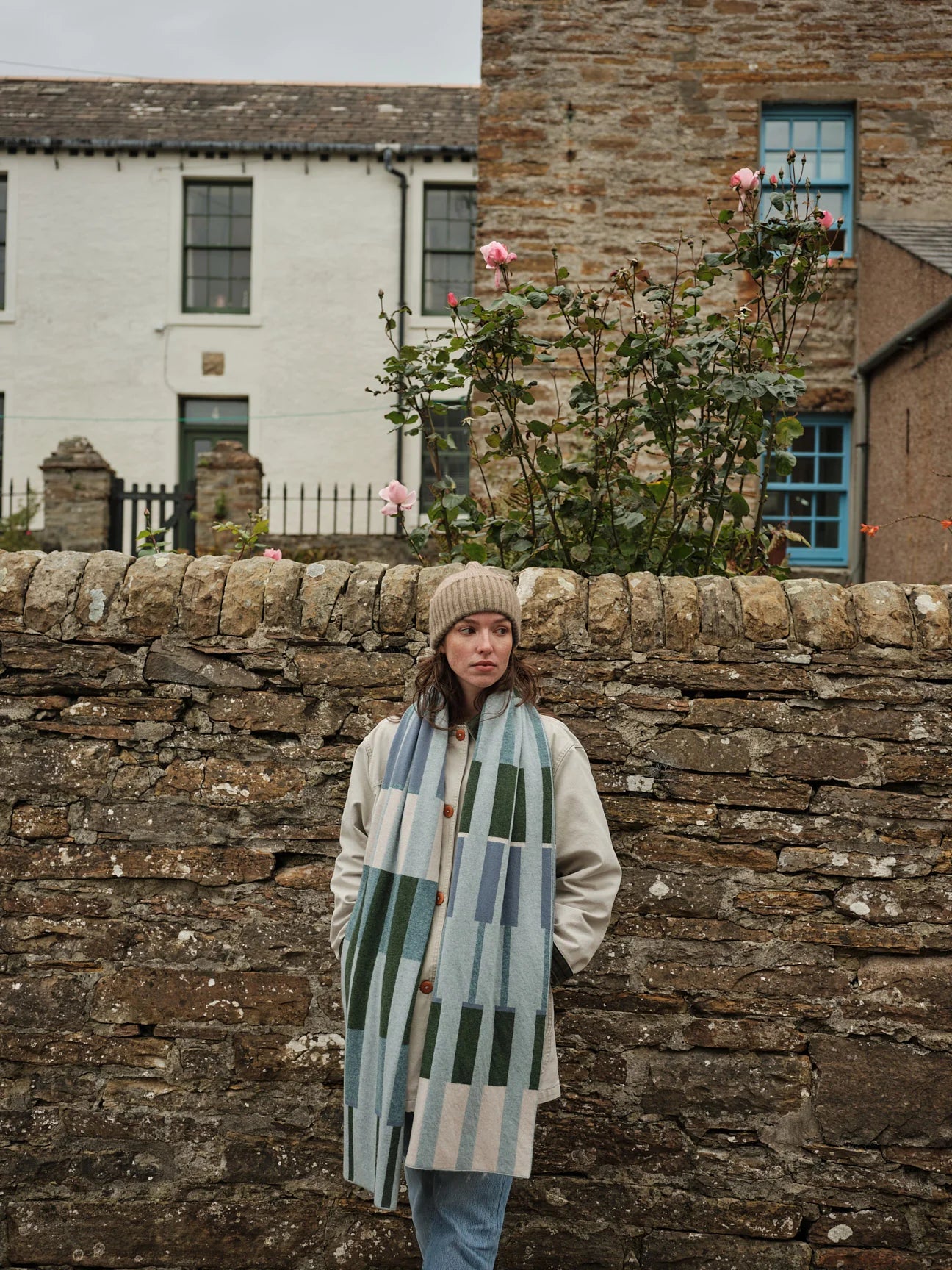 Woman standing in front of a stone wall with a house in the background