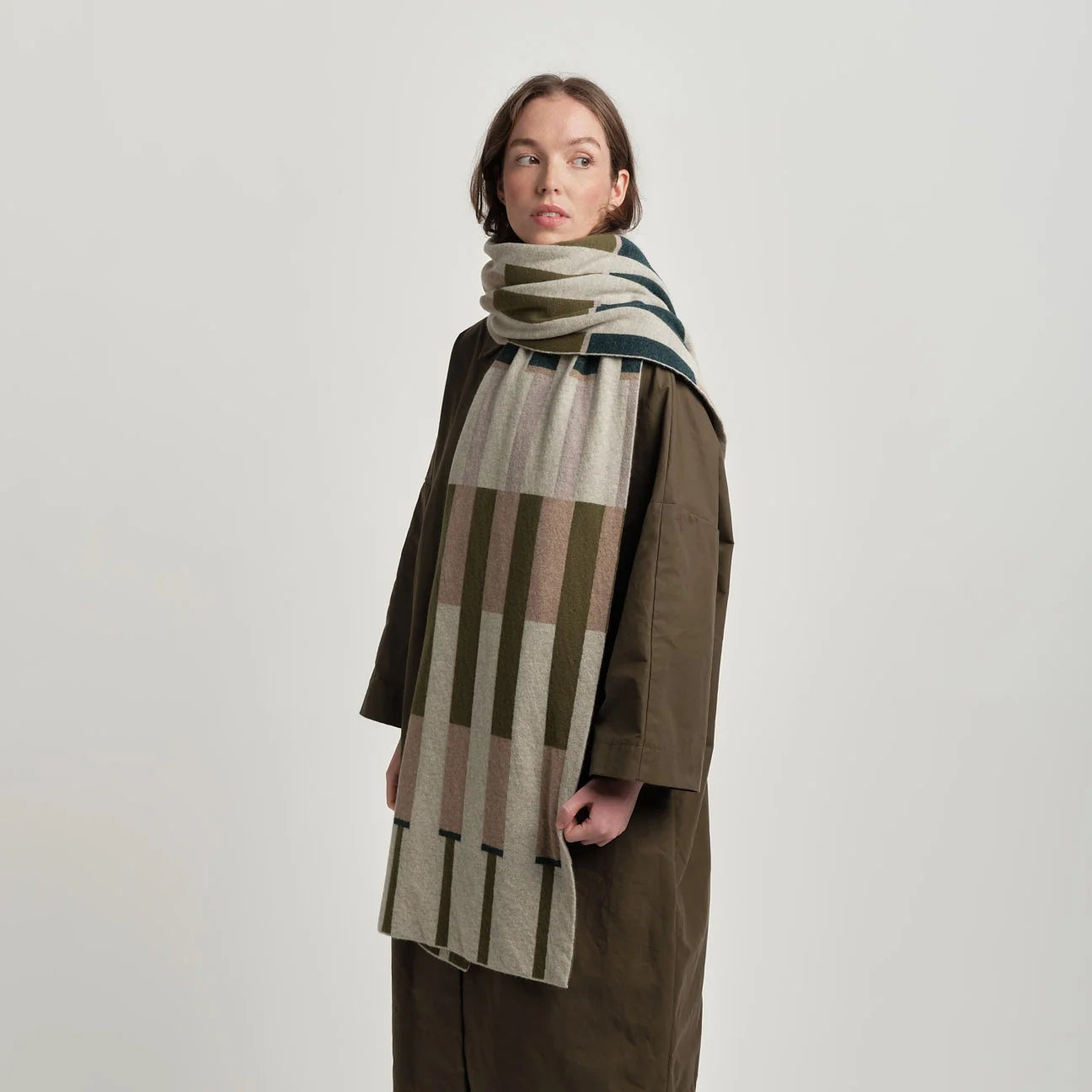 Person wearing a long coat and striped scarf on a white background