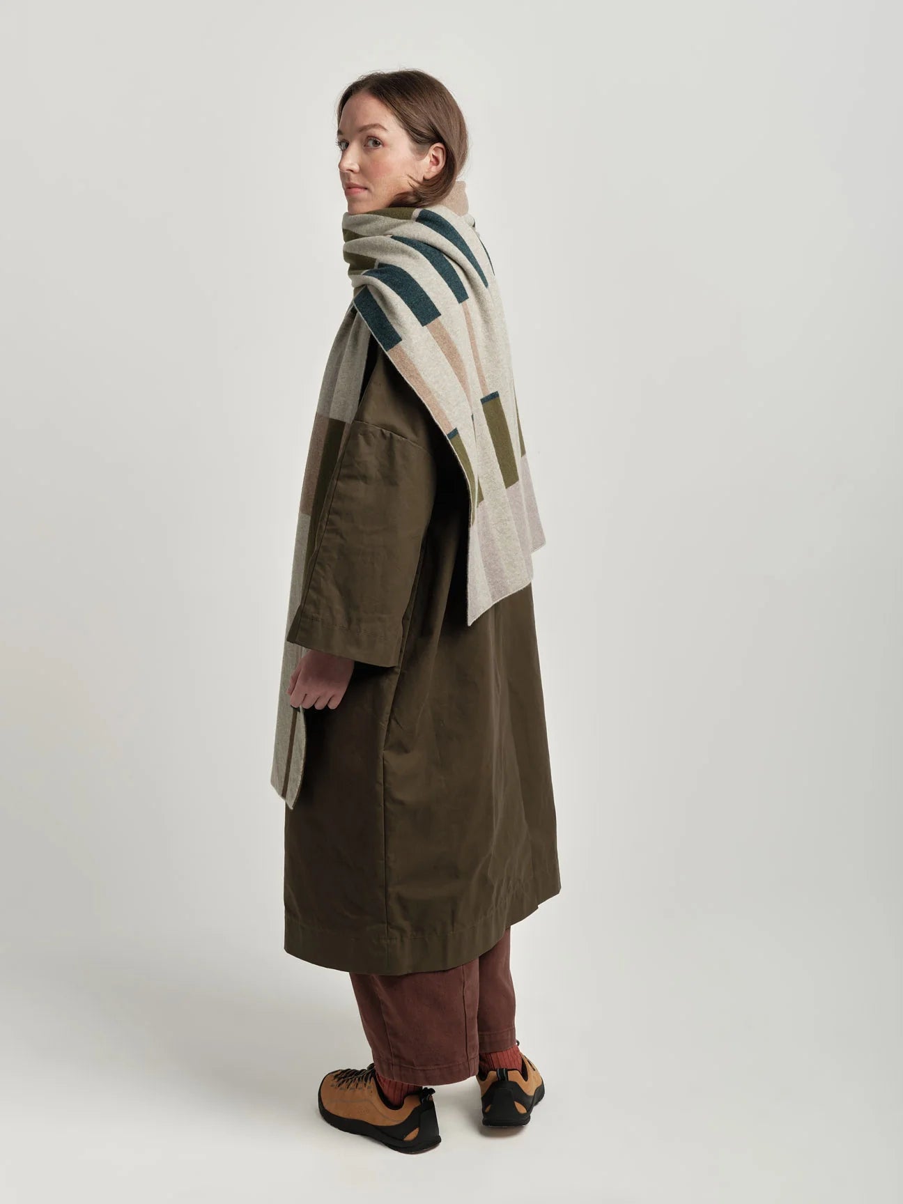 Person wearing a long coat and patterned scarf on a white background