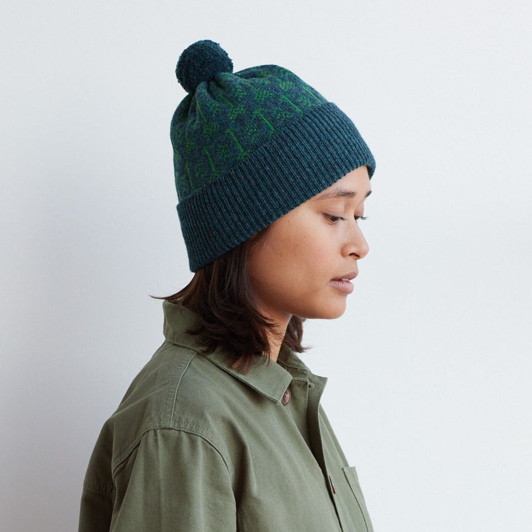 Teal knit beanie with a pompom and a subtle green patterned design.