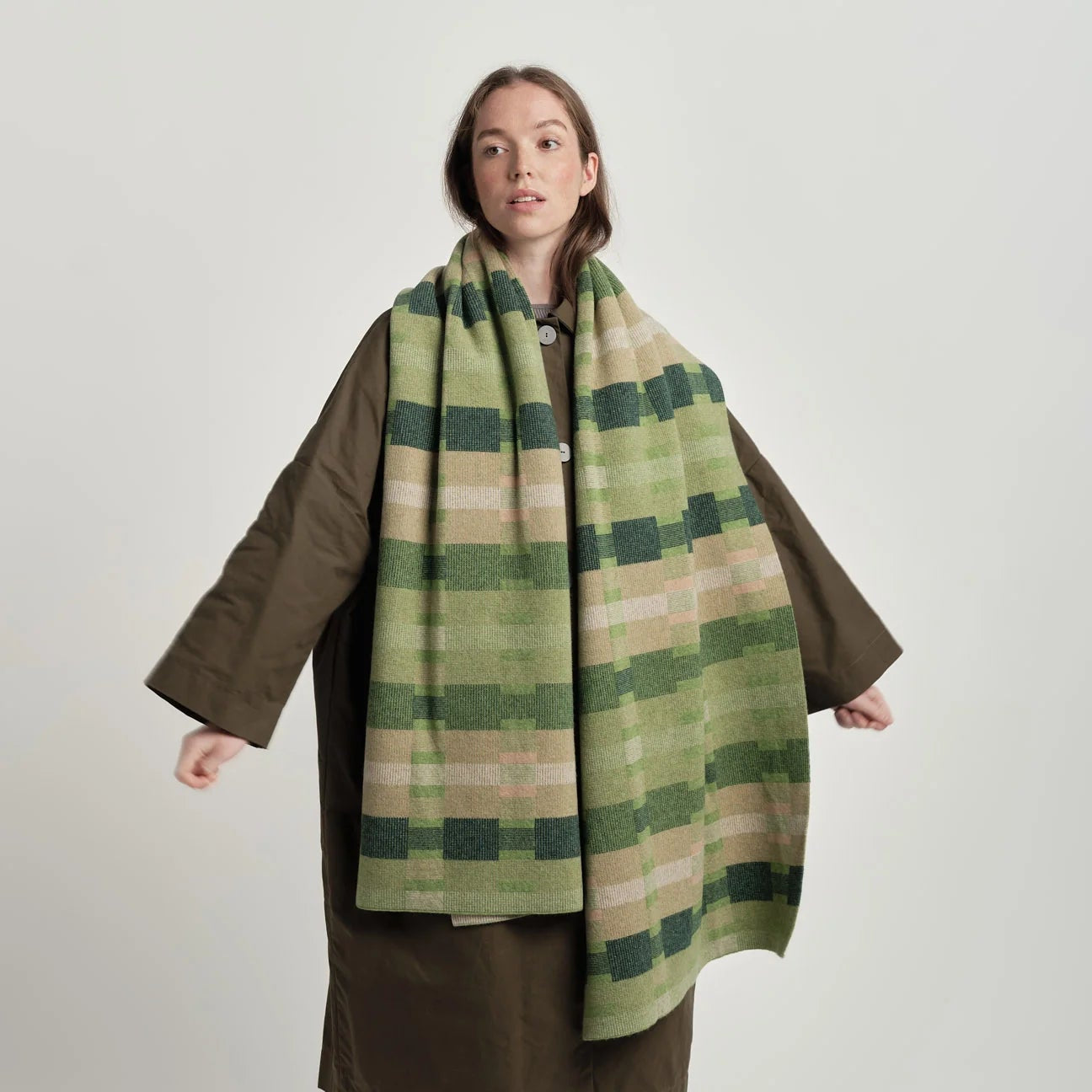 Person wearing a green plaid scarf and brown coat on a white background
