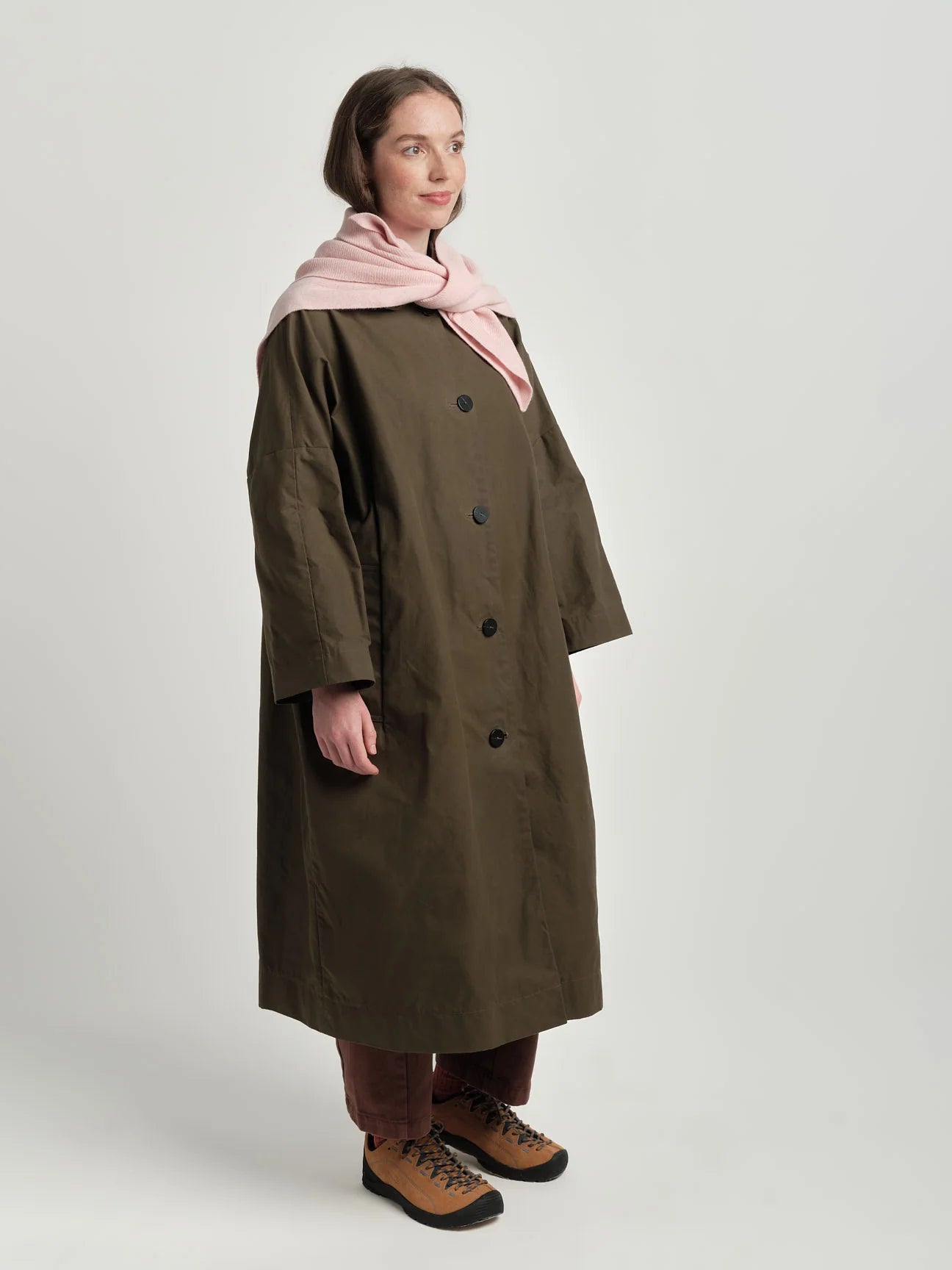 Person wearing a long dark coat with a pink scarf on a white background