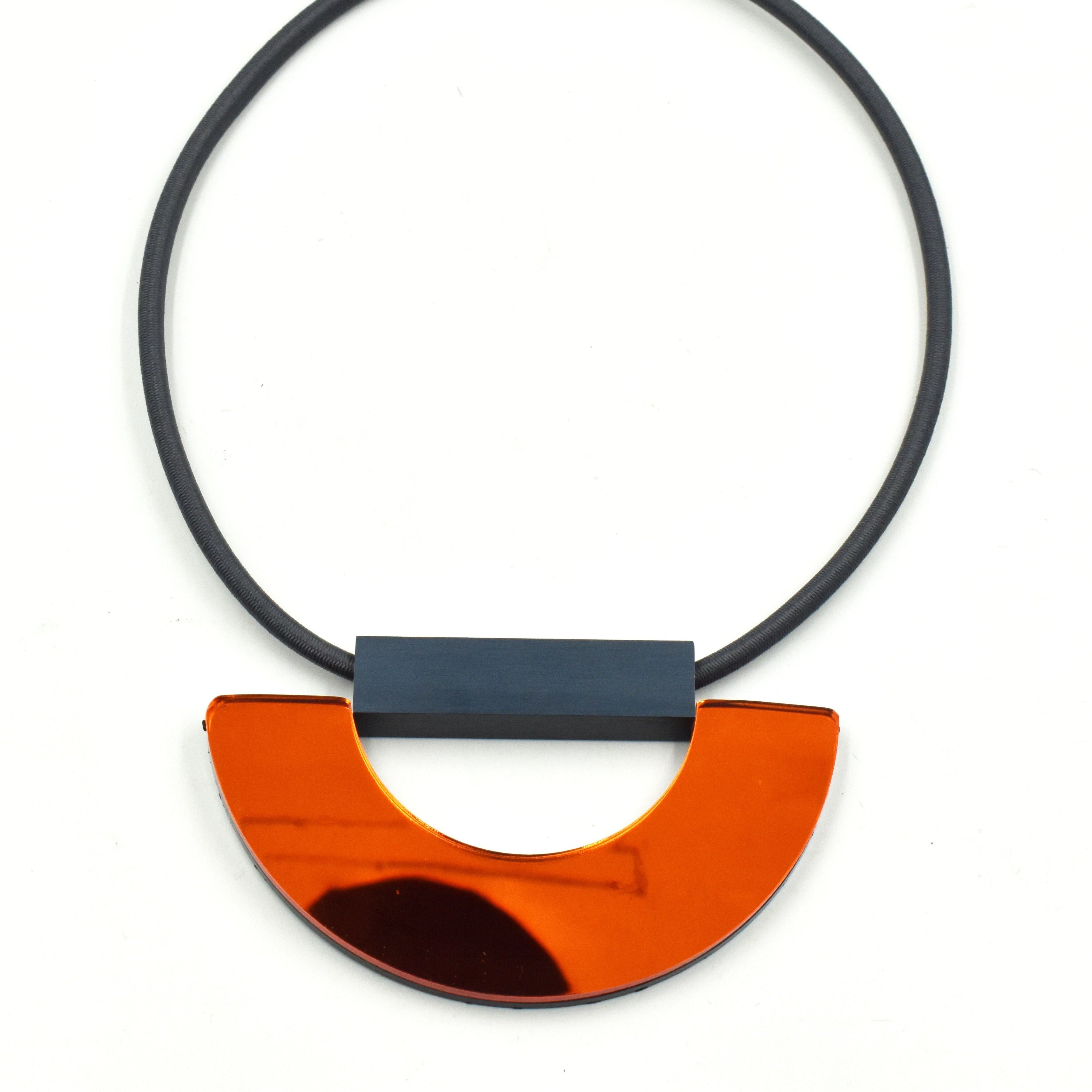 Modern necklace with a dark gray cord and a bright orange, semi-circular pendant.