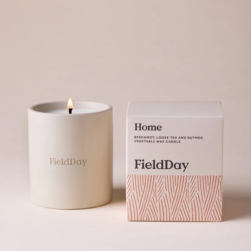 White candle with 'FieldDay' branding next to its packaging on a beige background