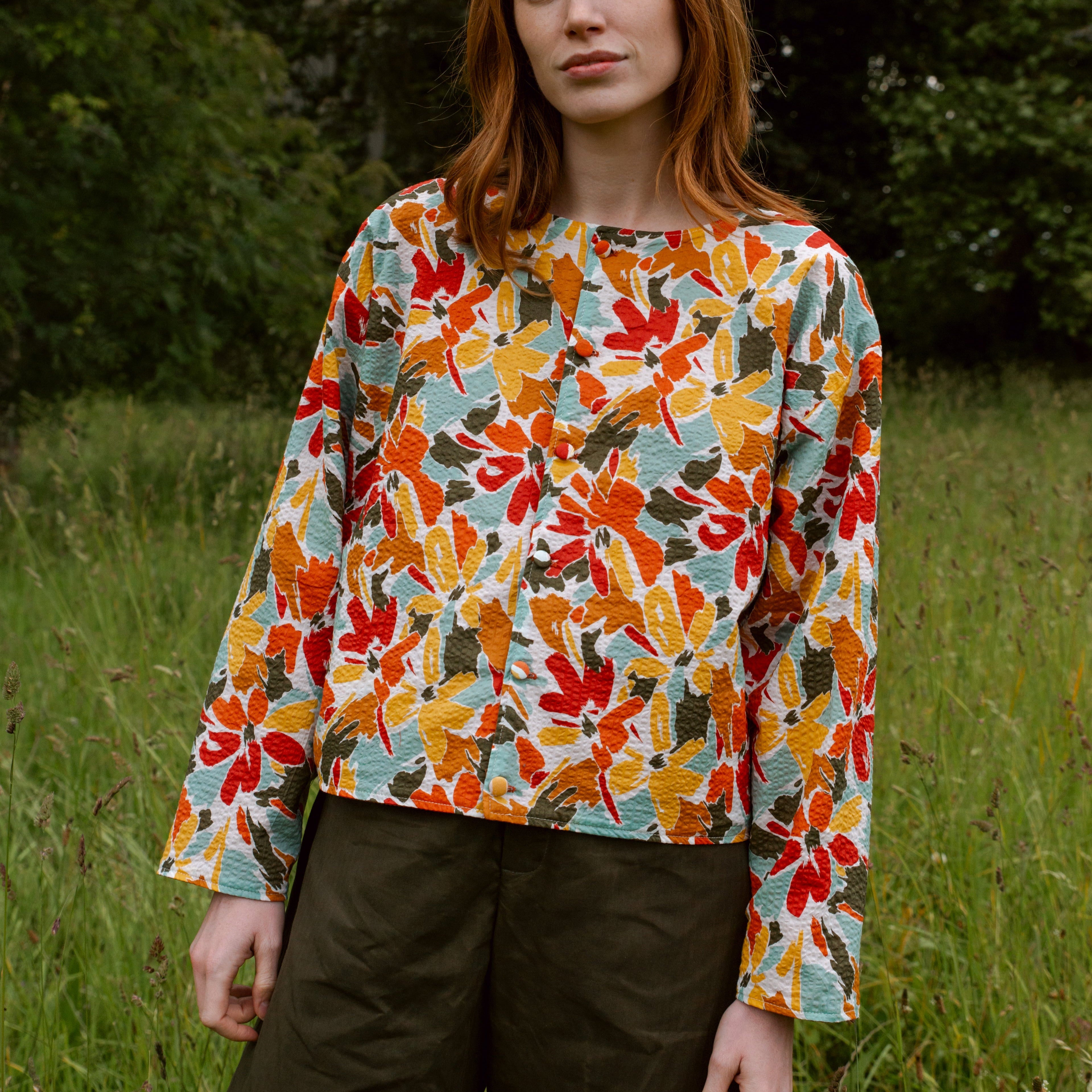 A women's long-sleeved button-up shirt with a vibrant abstract floral print in orange, red, yellow, and teal on a white