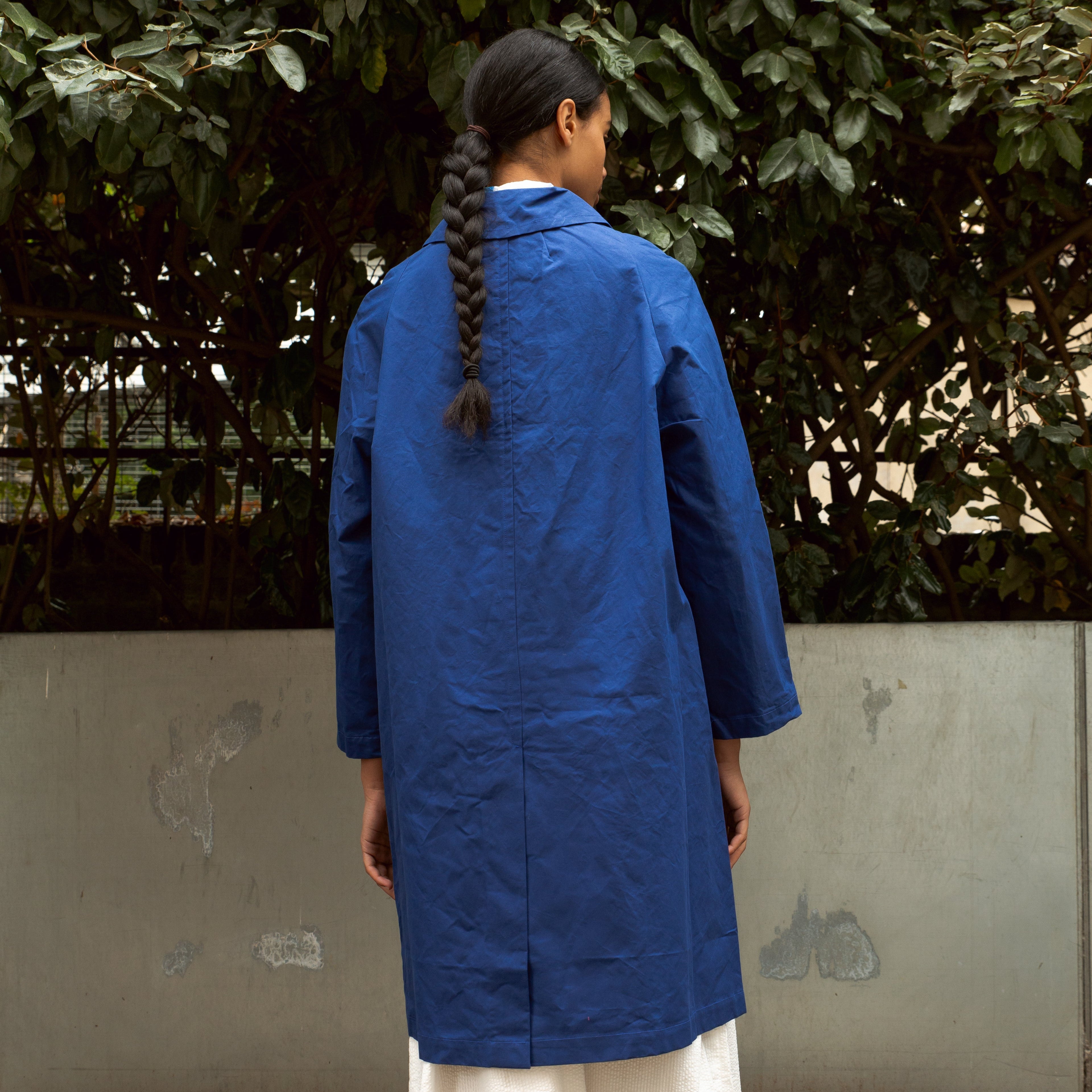 Rear view of a long, cobalt blue, collared coat.  The coat is knee-length with long sleeves and a center back seam.