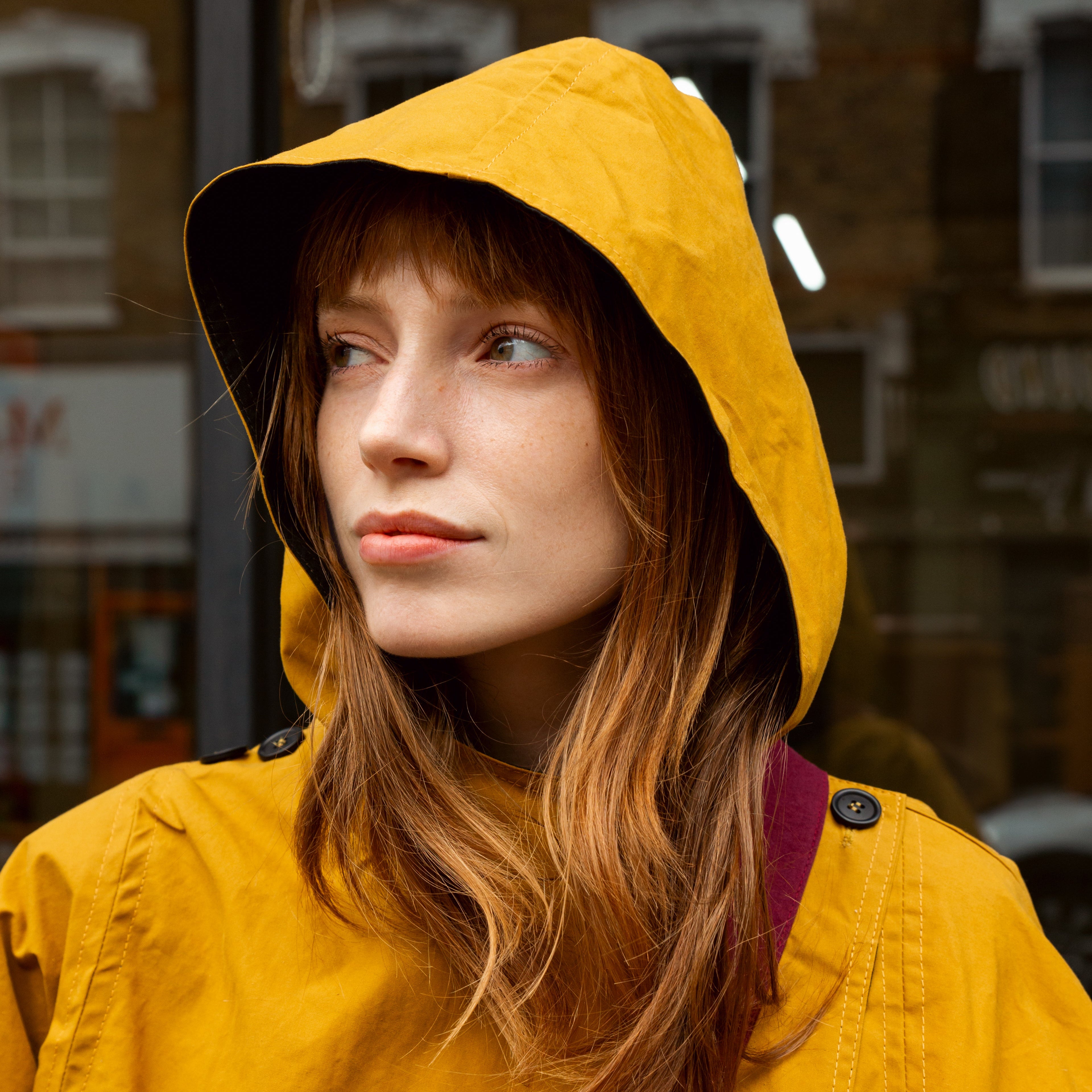 Woman with long auburn hair wearing a mustard yellow hooded raincoat.