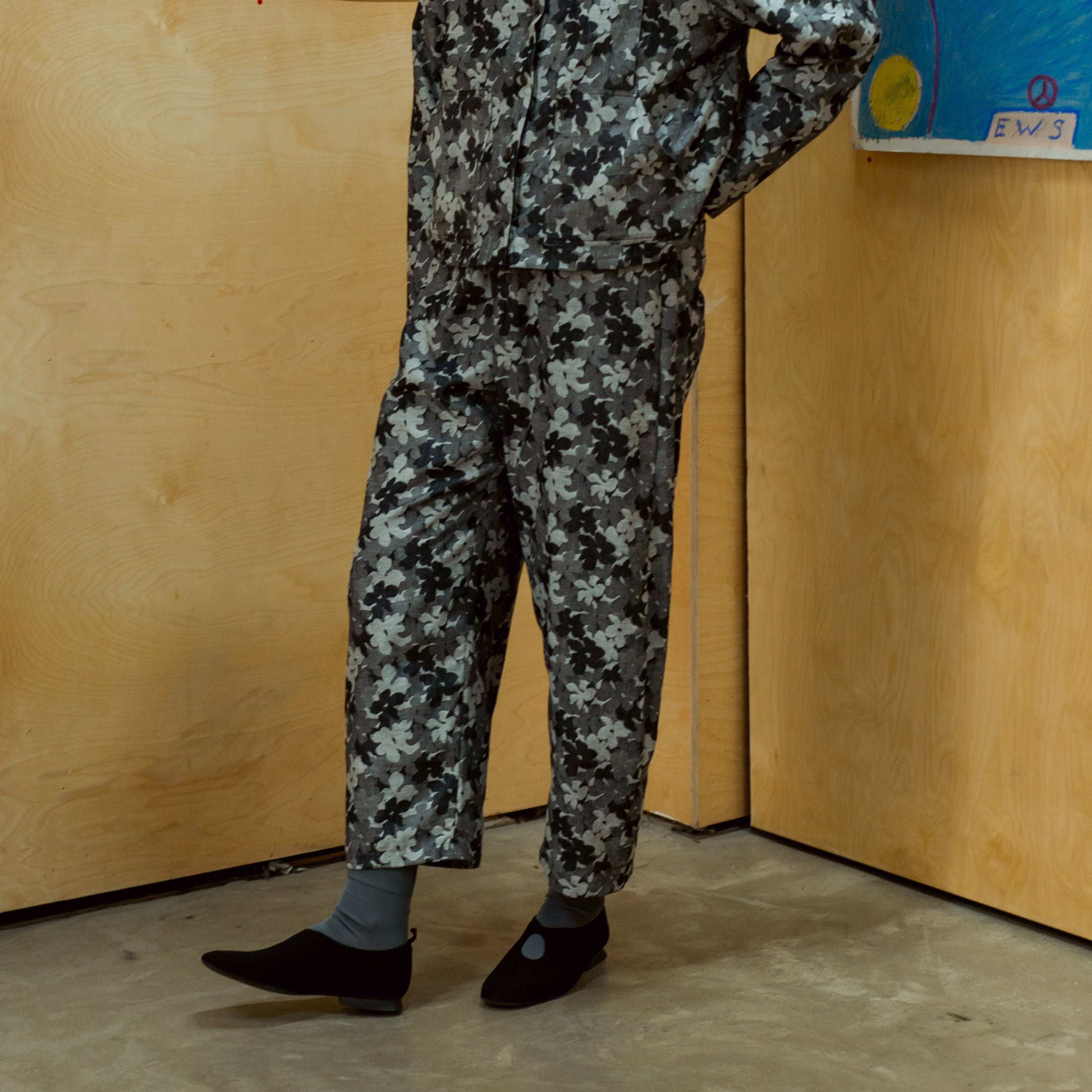 Black slip-on shoes and wide-leg trousers with a grey and black abstract floral print.