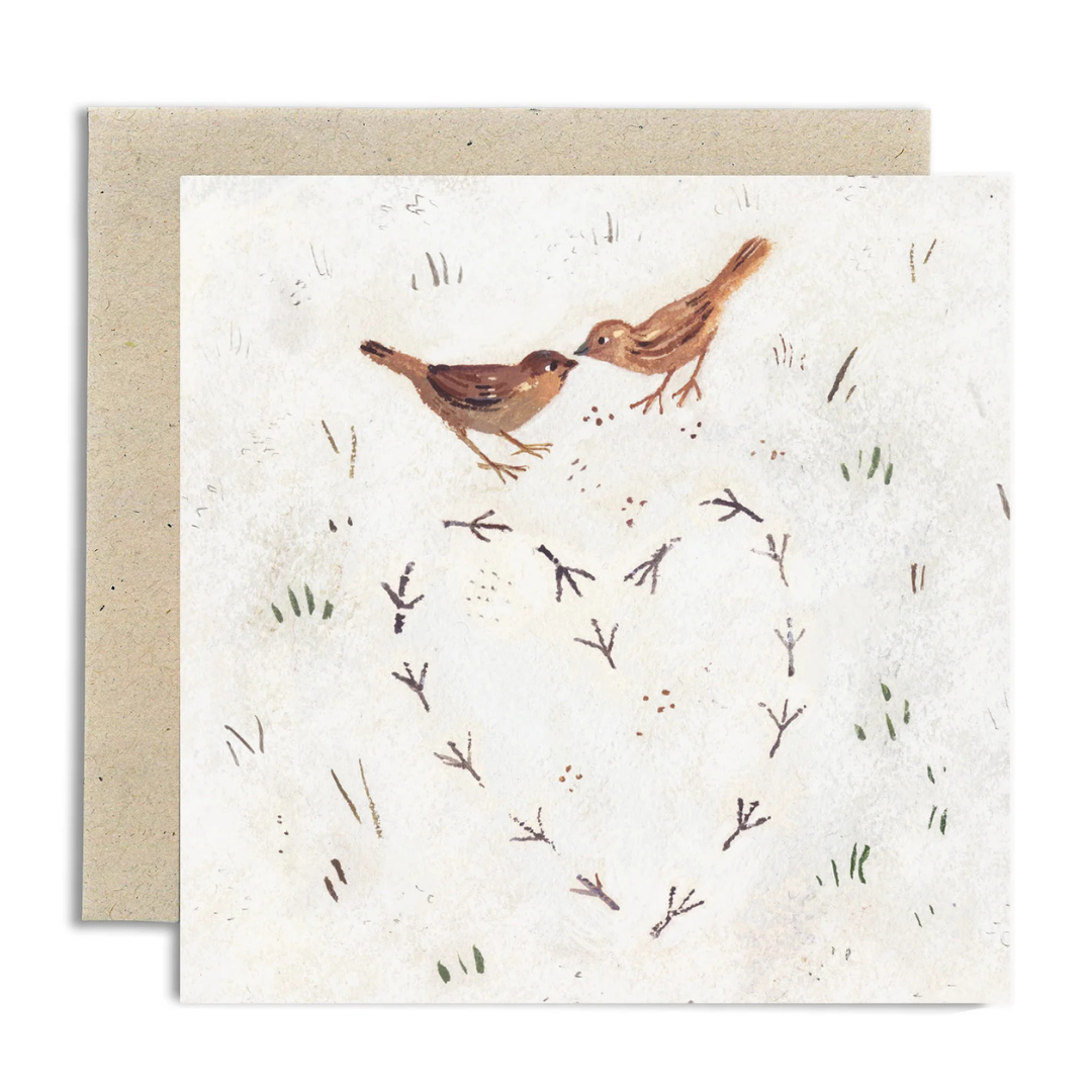 A square greeting card with a kraft envelope behind it, featuring a watercolor-style illustration of two small brown birds facing each other above a heart-shaped arrangement of bird footprints on an off-white textured background.