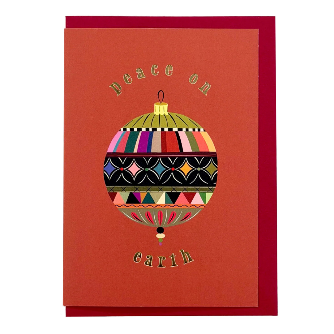 A red greeting card with a matching red envelope, featuring a colorful patterned Christmas ornament illustration and the words 'Peace on earth' in gold lettering.