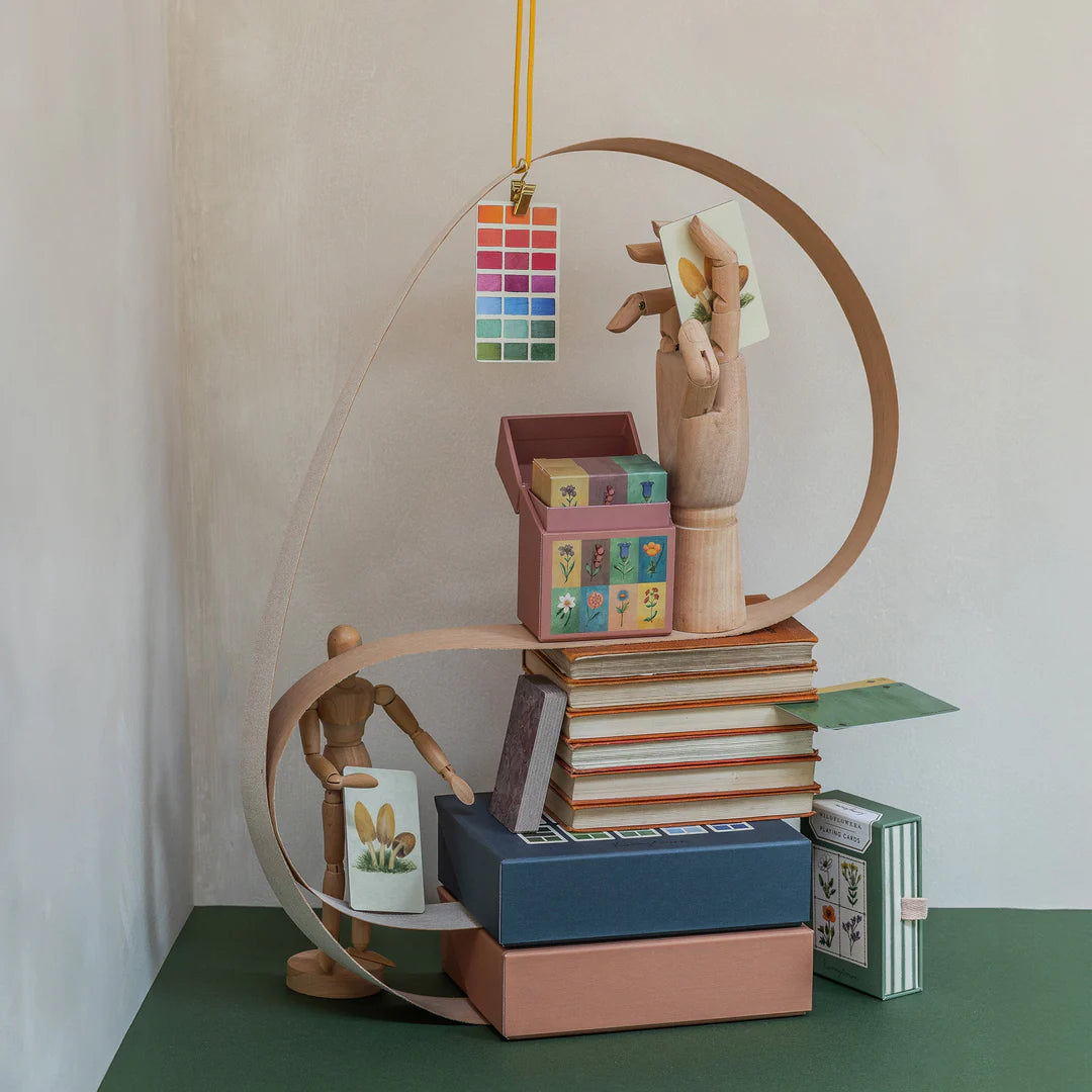 Wooden figures and books arranged on a circular shelf against a plain wall.