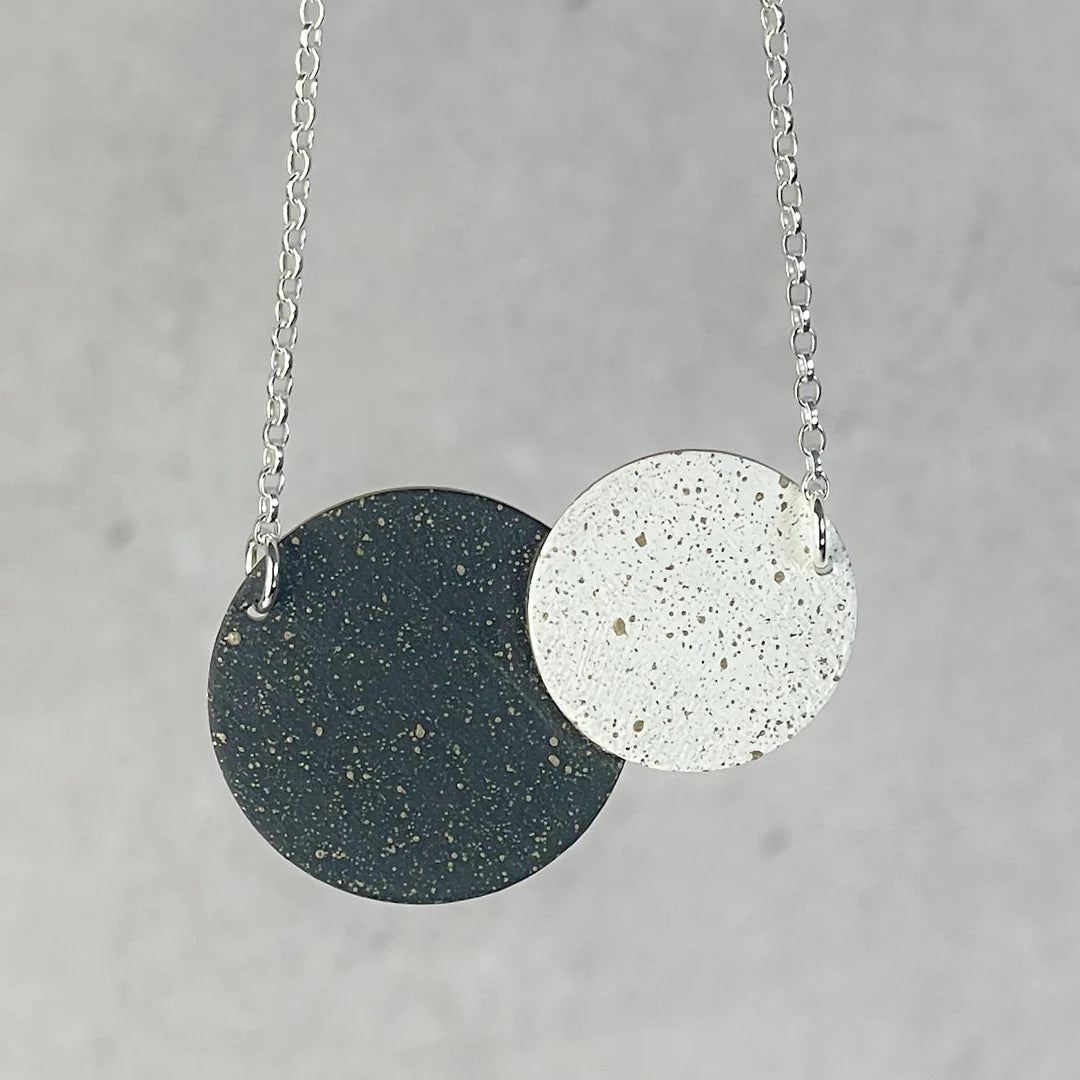 Necklace with two overlapping speckled discs; one dark green, one white, on a silver chain.