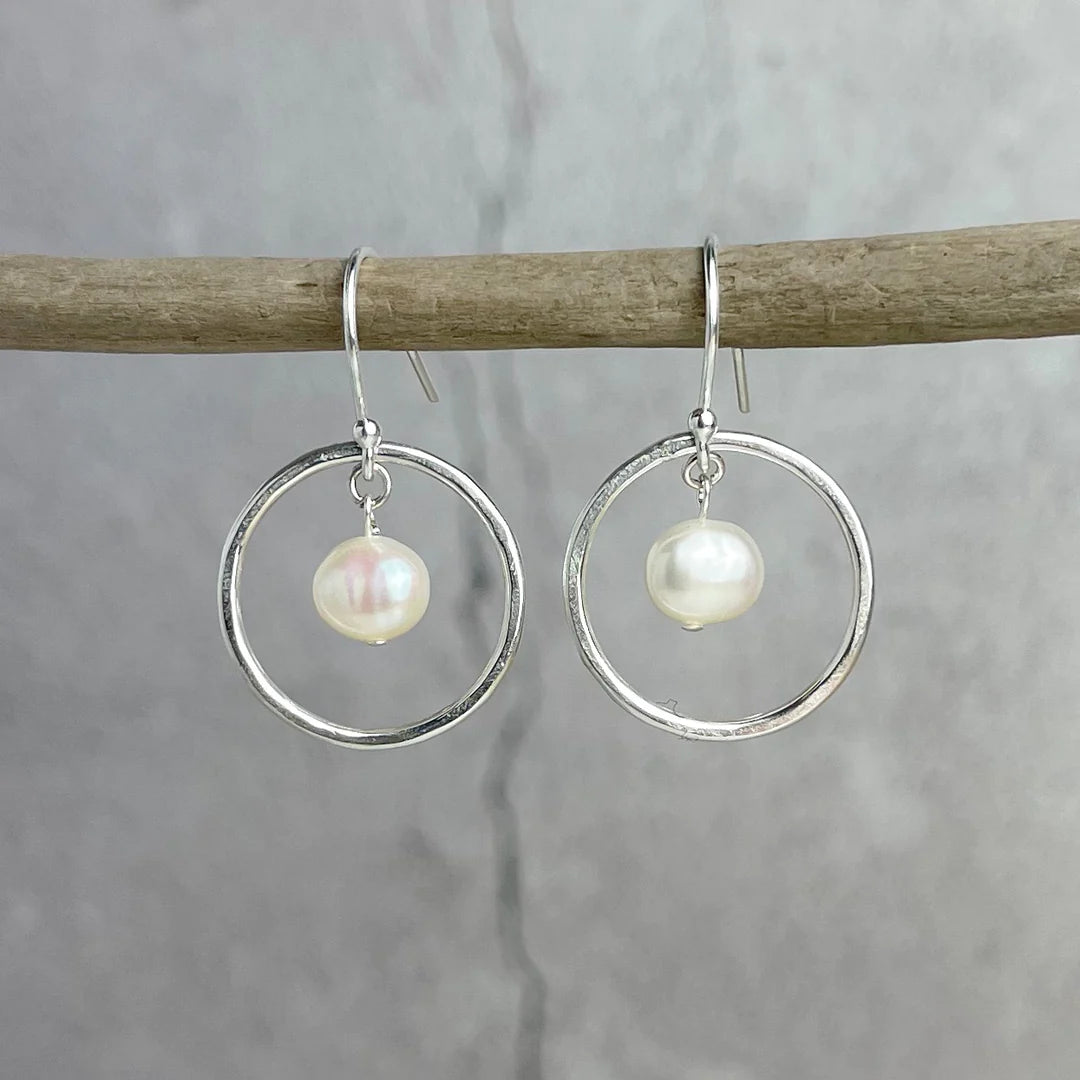 Silver hoop earrings with a single pearl dangling from each hoop.