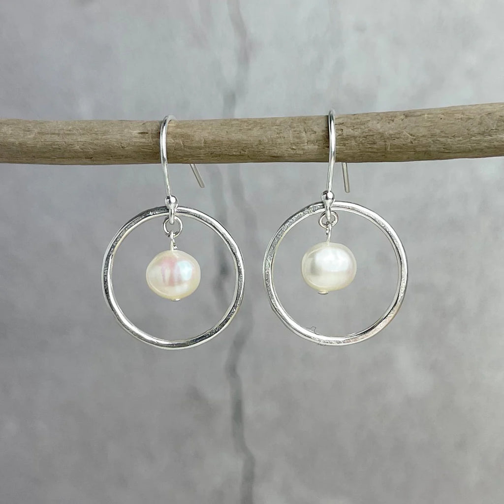 Silver hoop earrings with a single pearl dangling from each hoop.