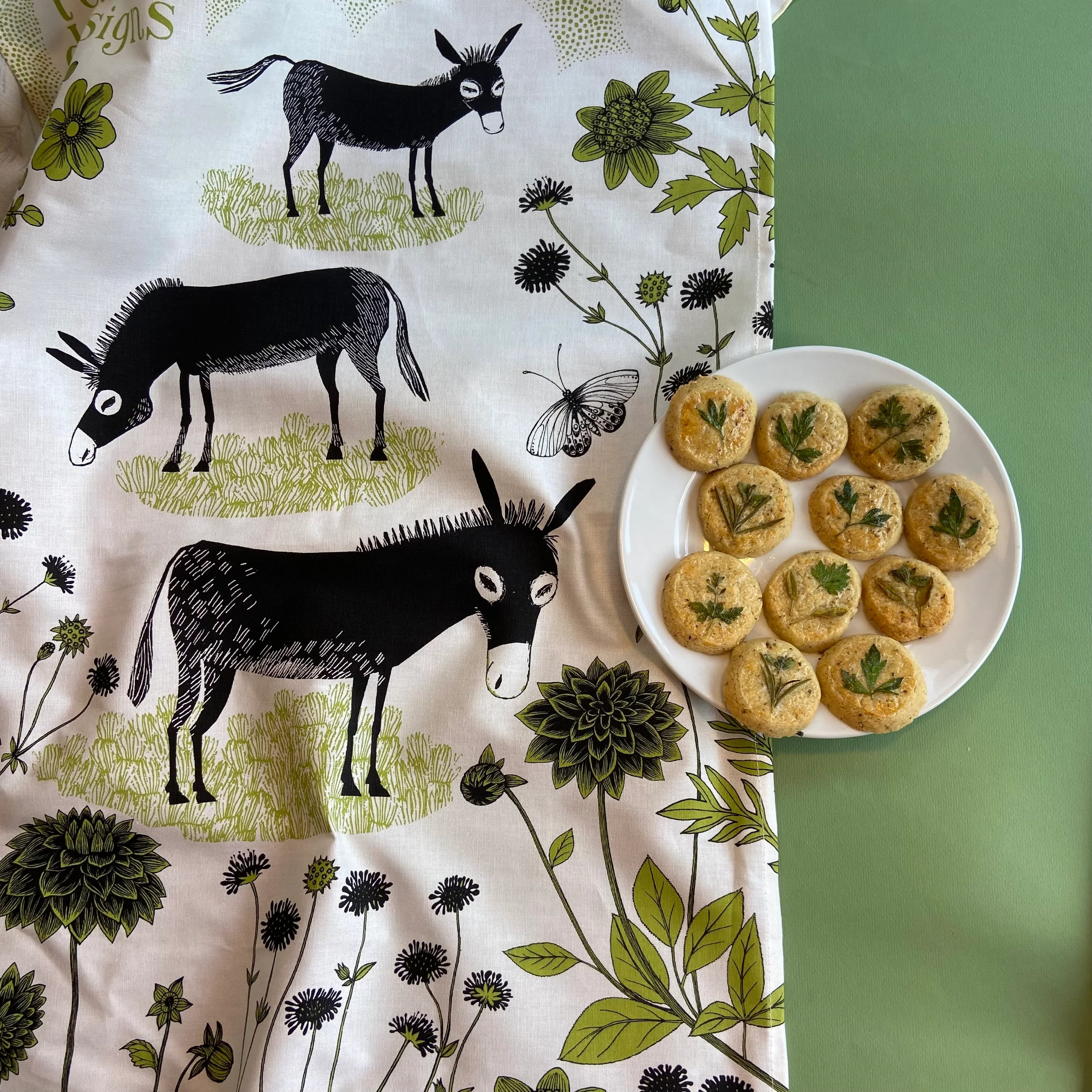 A plate of round, pale-golden cookies, each topped with a small sprig of herbs.