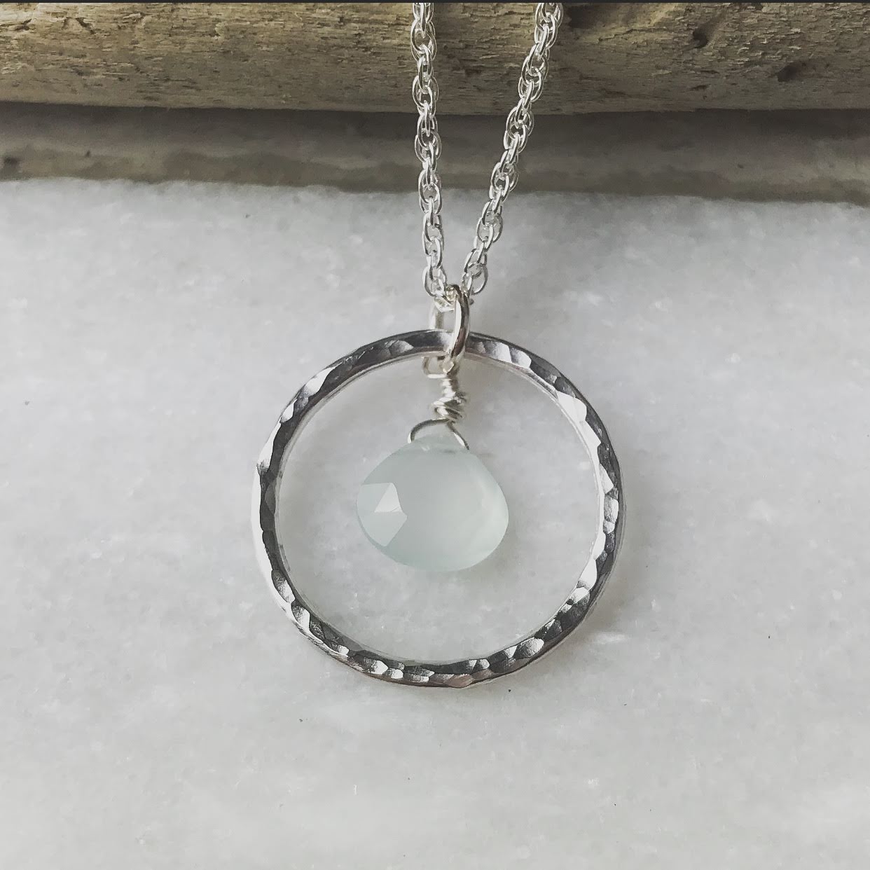 Silver chain necklace with hammered circular pendant featuring a pale green gemstone.