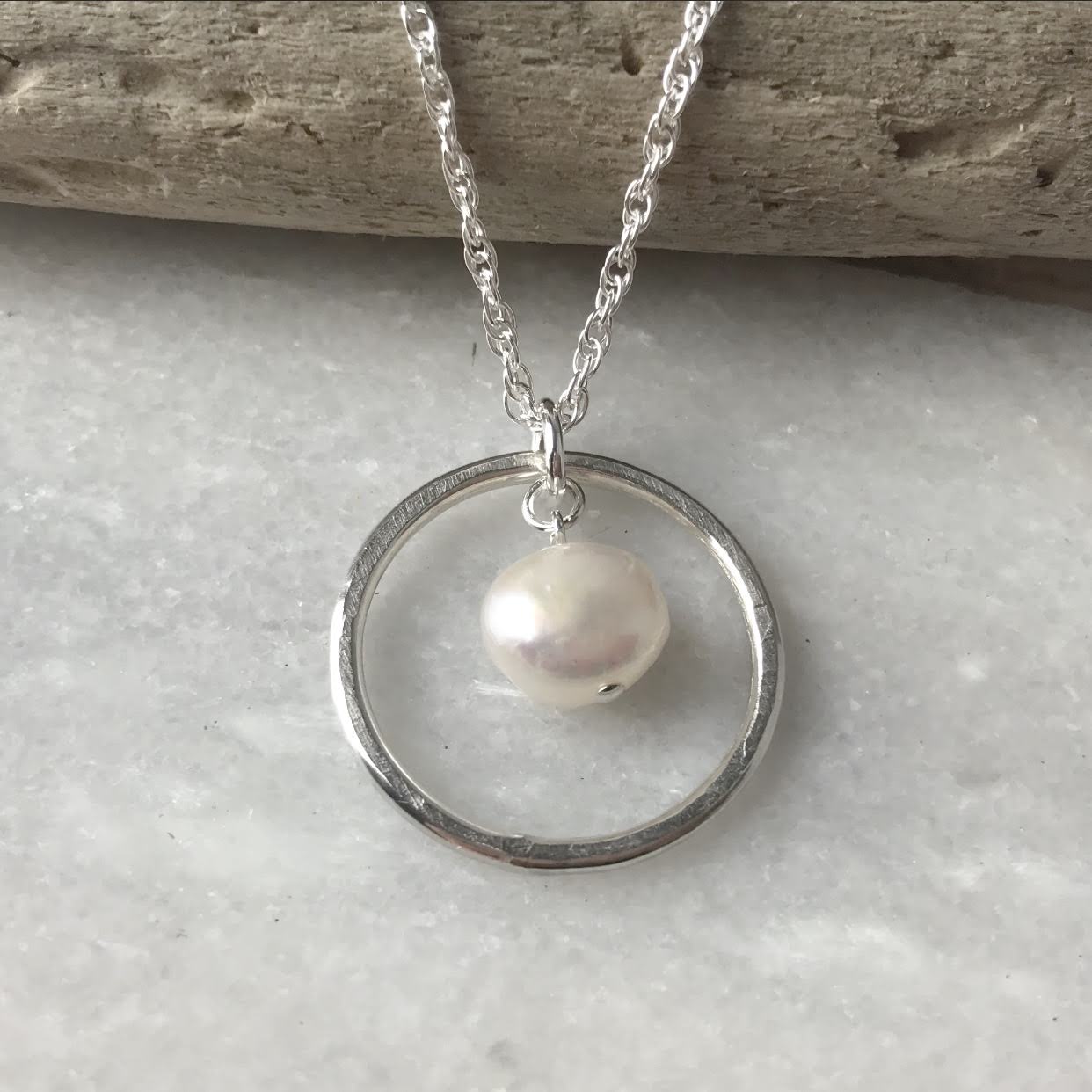 Silver chain necklace with a single white pearl pendant encircled by a minimalist silver ring.