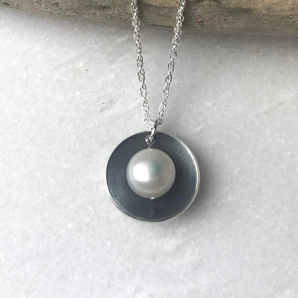 Silver necklace featuring a round, dark gray pendant with a single white pearl centered on it.