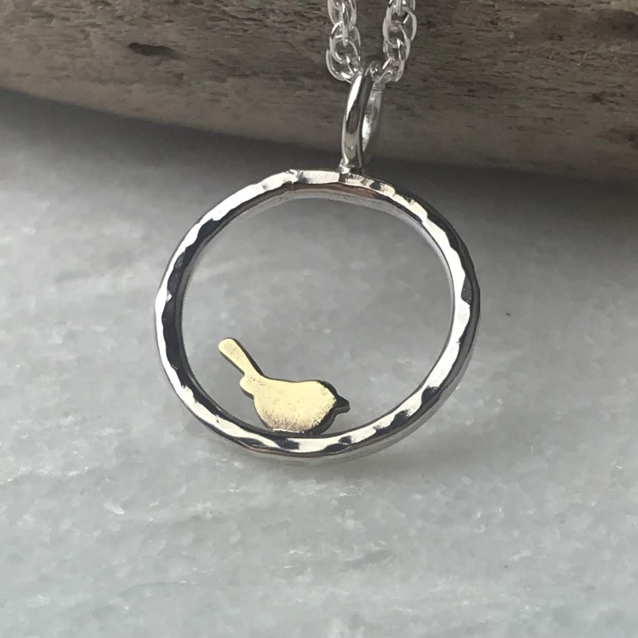 Silver necklace with hammered circular pendant featuring a small gold bird.