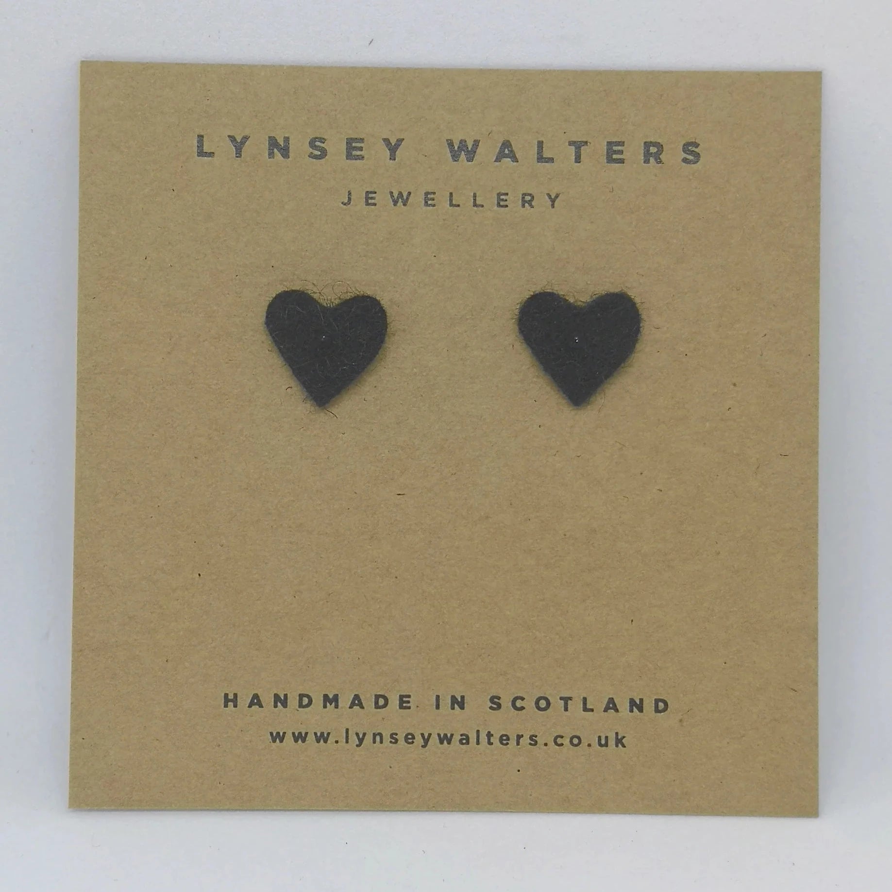 Pair of black felt heart-shaped stud earrings displayed on a brown card.