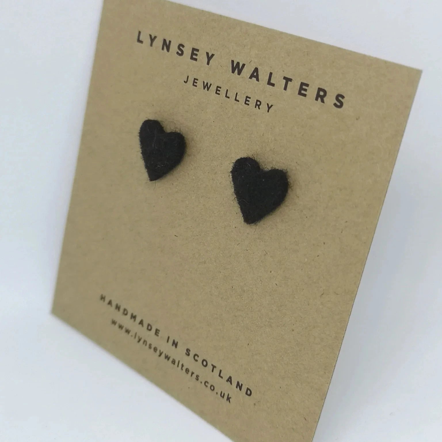 Pair of black felt heart stud earrings displayed on a brown card.