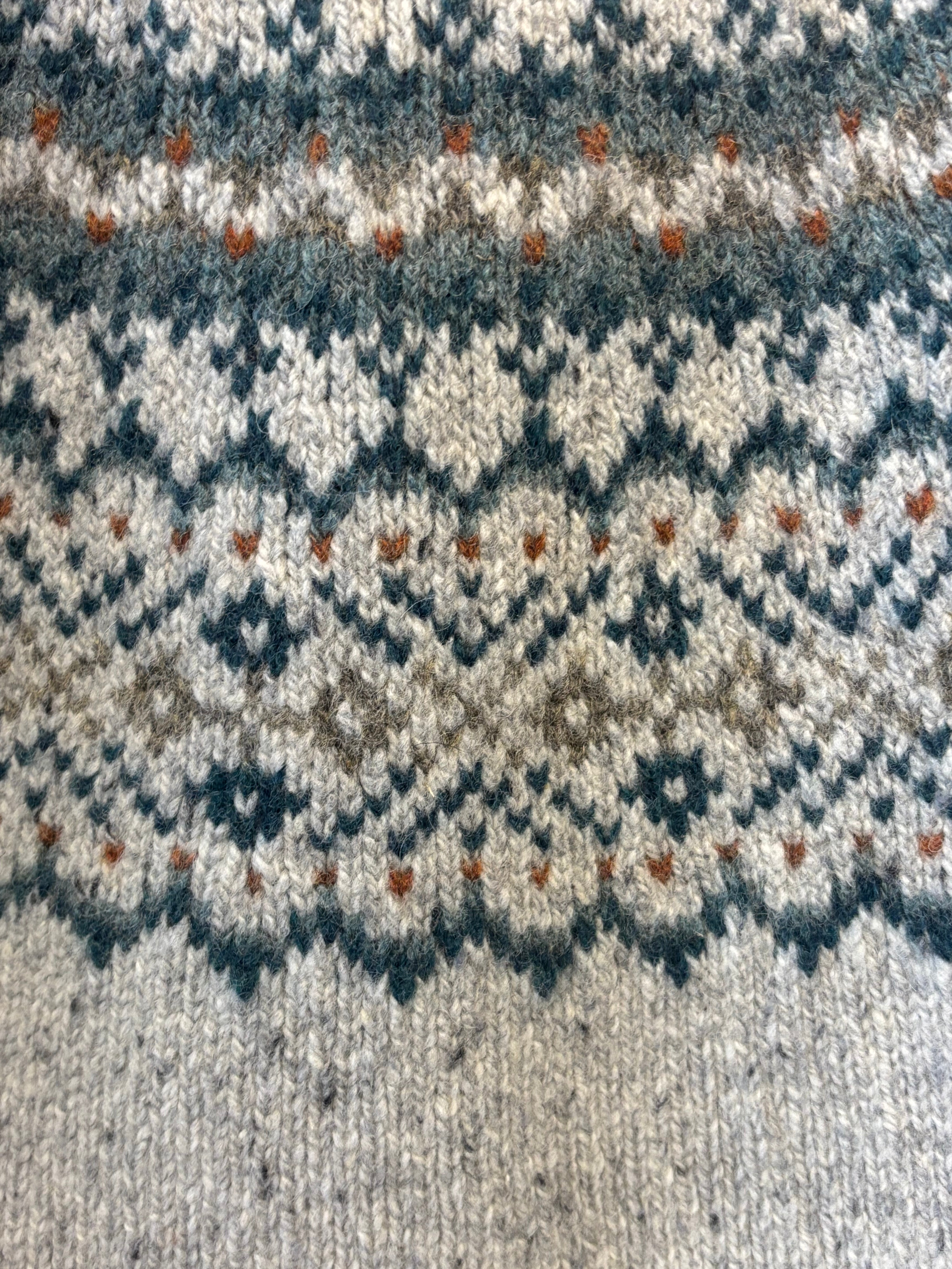 Close-up of hand-knitted wool fabric with a teal, gray, and brown Fair Isle pattern.