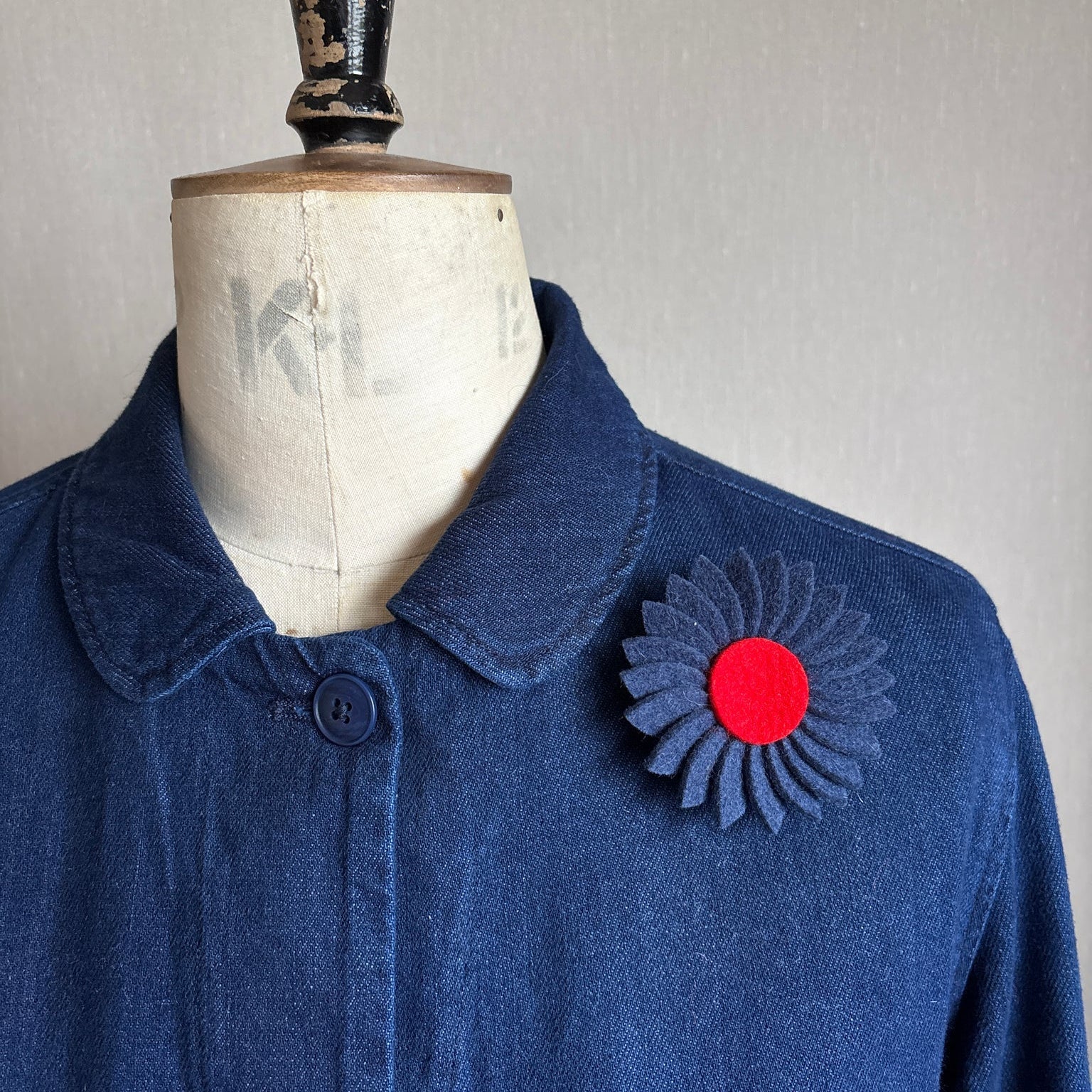 Blue coat with a red and black flower brooch on a mannequin against a plain background