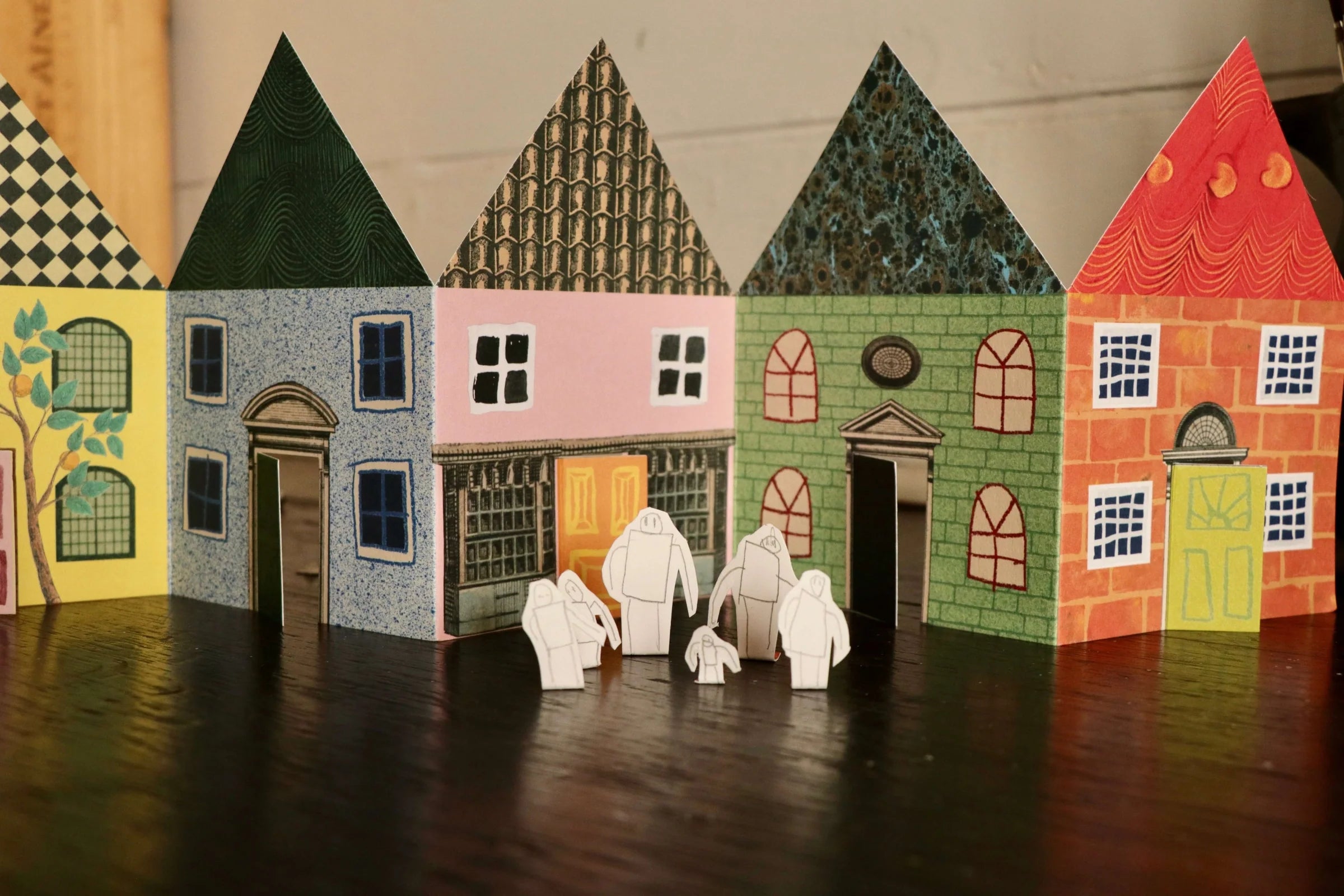 Row of colorful paper houses with cut-out doors and windows, and small paper figures standing in front.