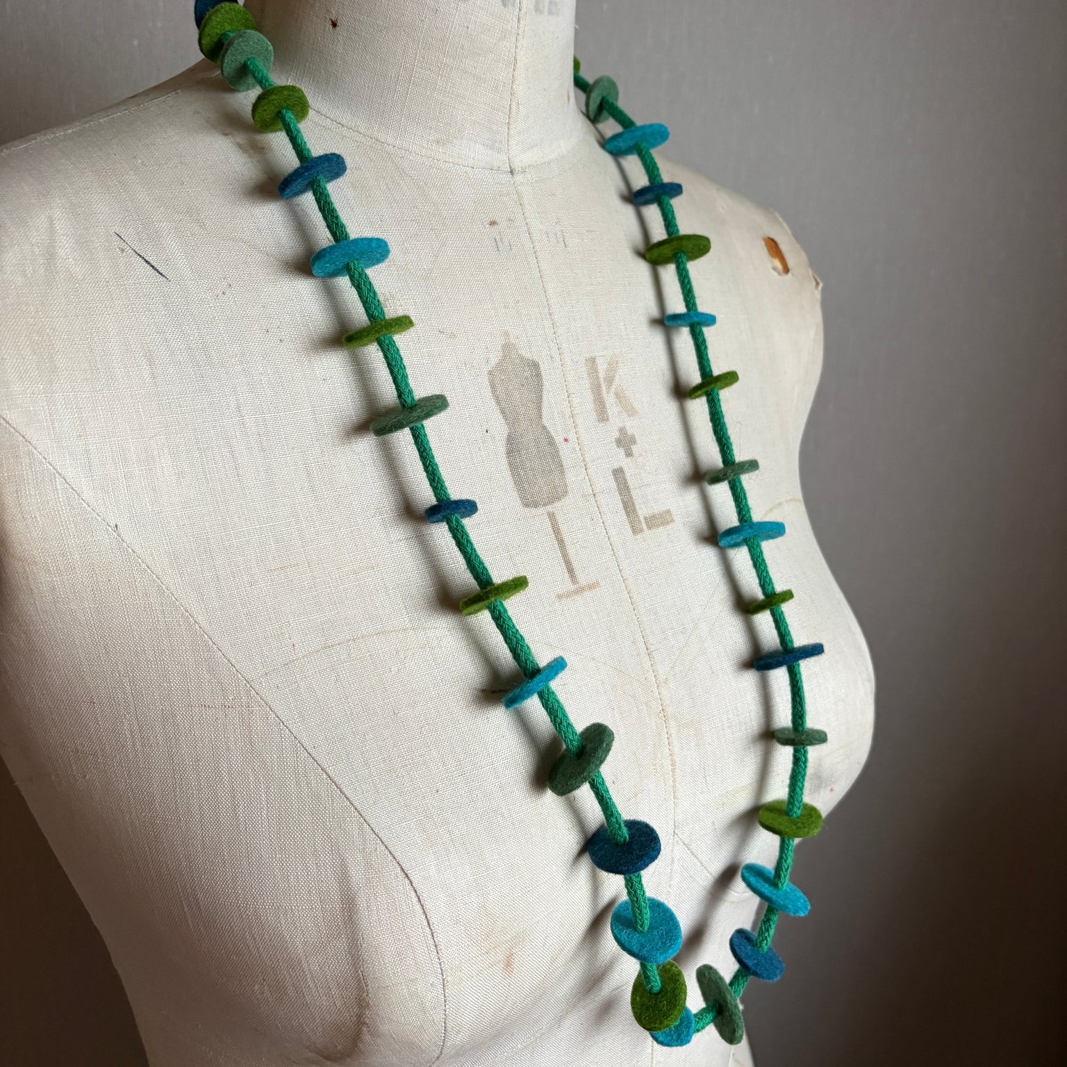 Necklace with green and blue beads on a mannequin bust against a plain background