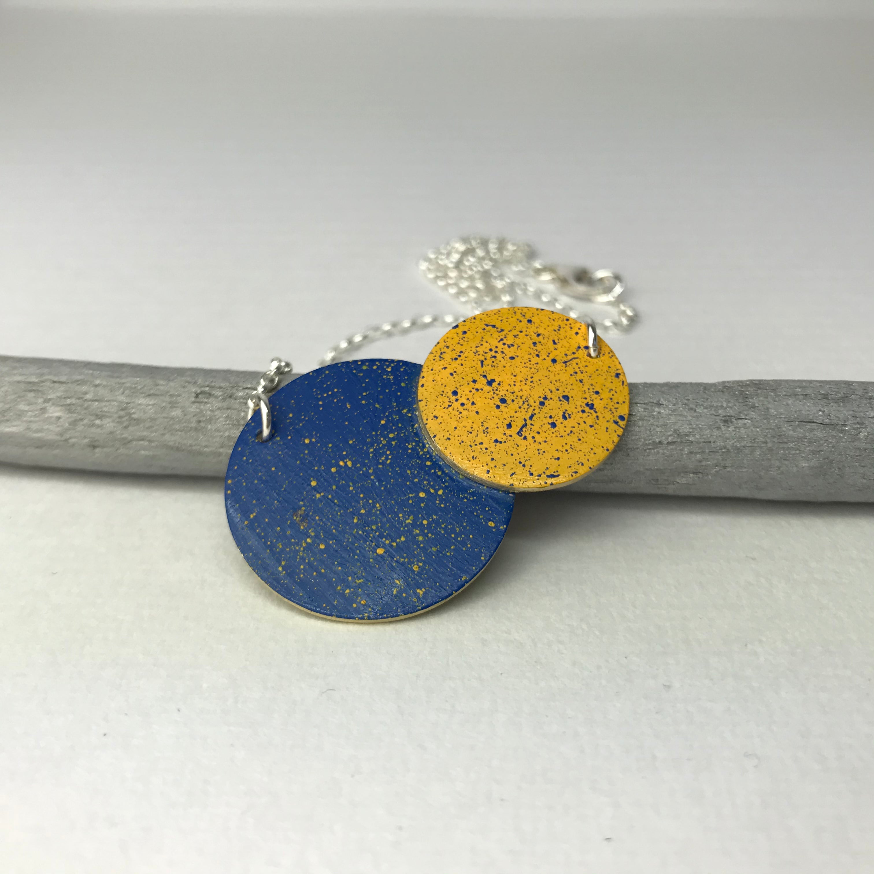 Necklace with two overlapping circular pendants; one blue, one gold; both with speckled detailing.