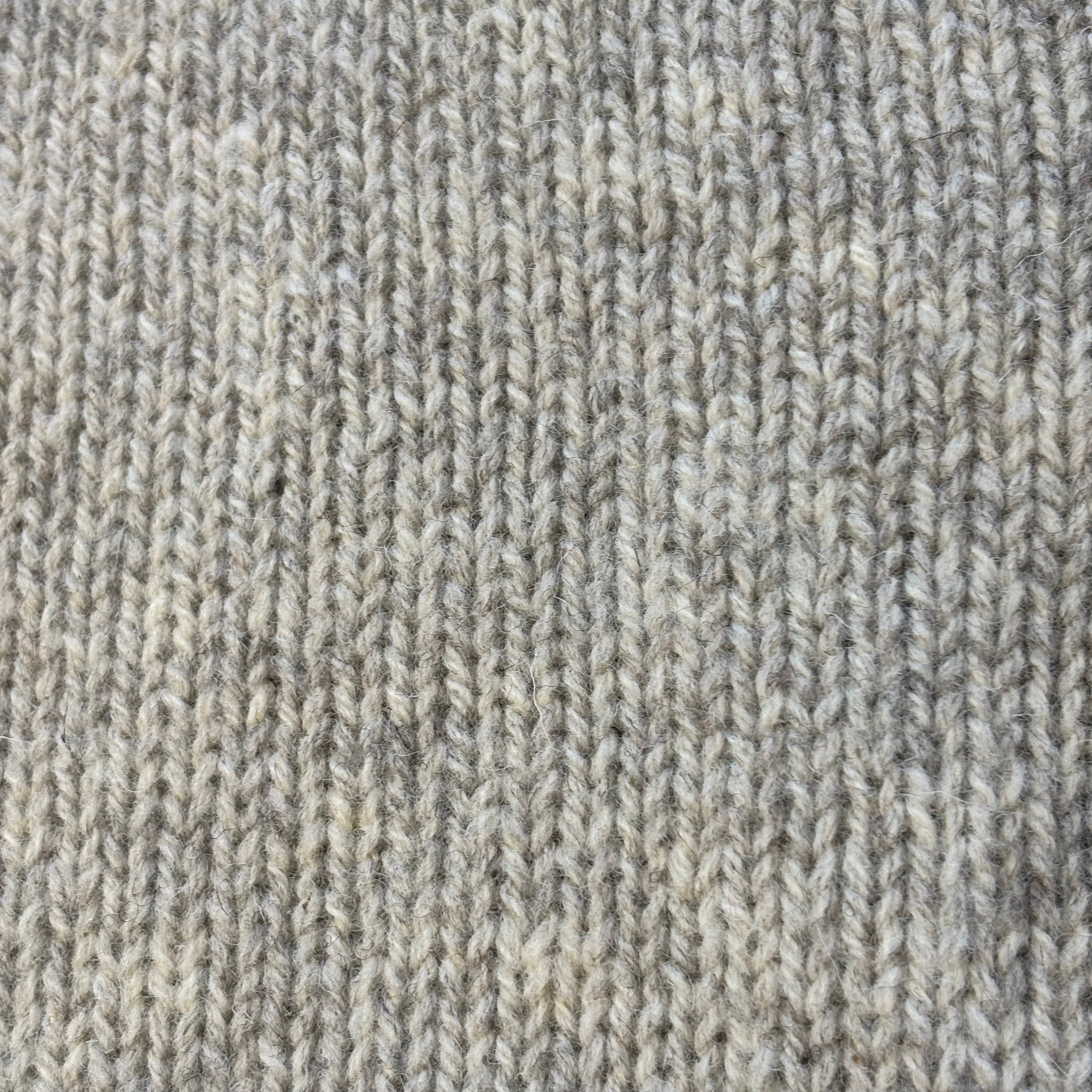 Close-up of a light gray knitted fabric with a textured, slightly fuzzy surface. The knit shows vertical lines of stitches.