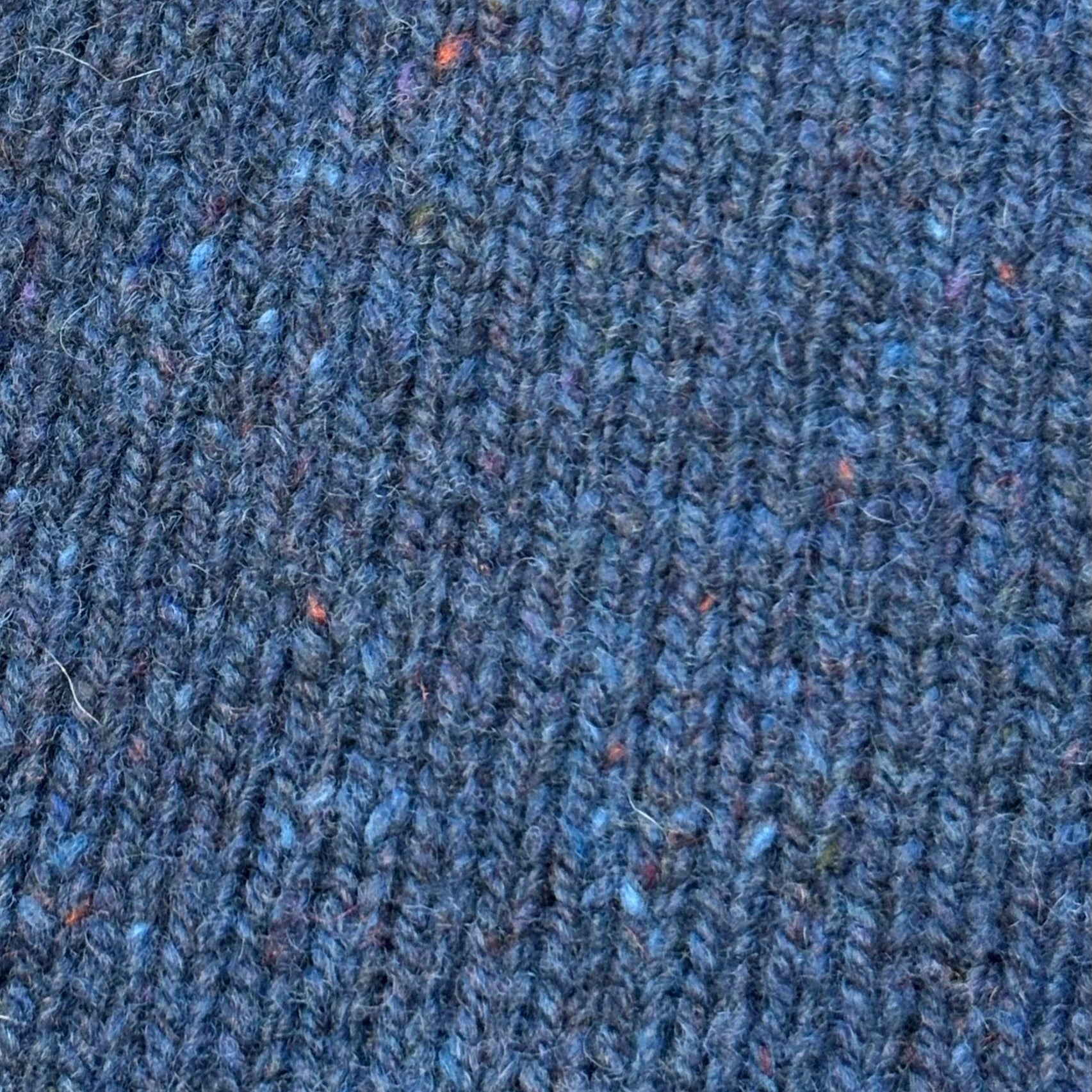 Close-up of a textured, dark blue knitted fabric with subtle flecks of other colors.